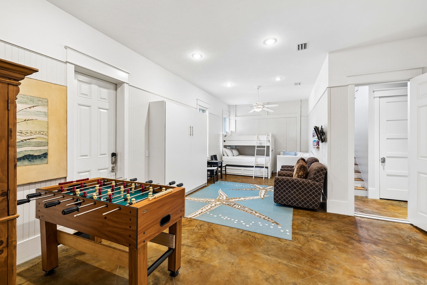 Your private game room awaits with foosball and cozy seating, opening to a spacious bedroom with bunk beds—perfect for family fun and relaxation under vaulted ceilings.