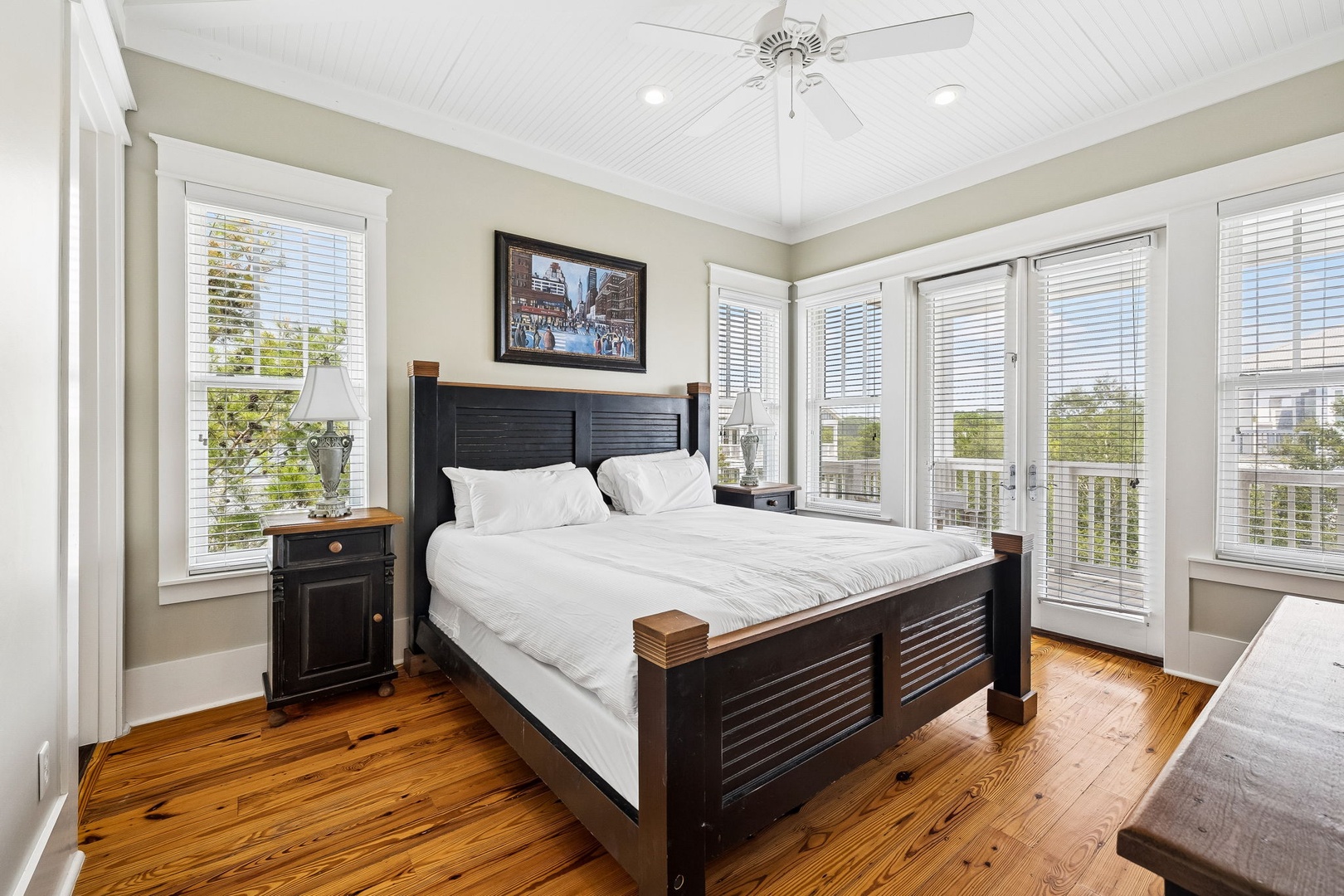 Bright, tranquil bedroom with polished hardwood floors, abundant natural light, and fresh white linens. French doors open to a private balcony for morning serenity and scenic views.