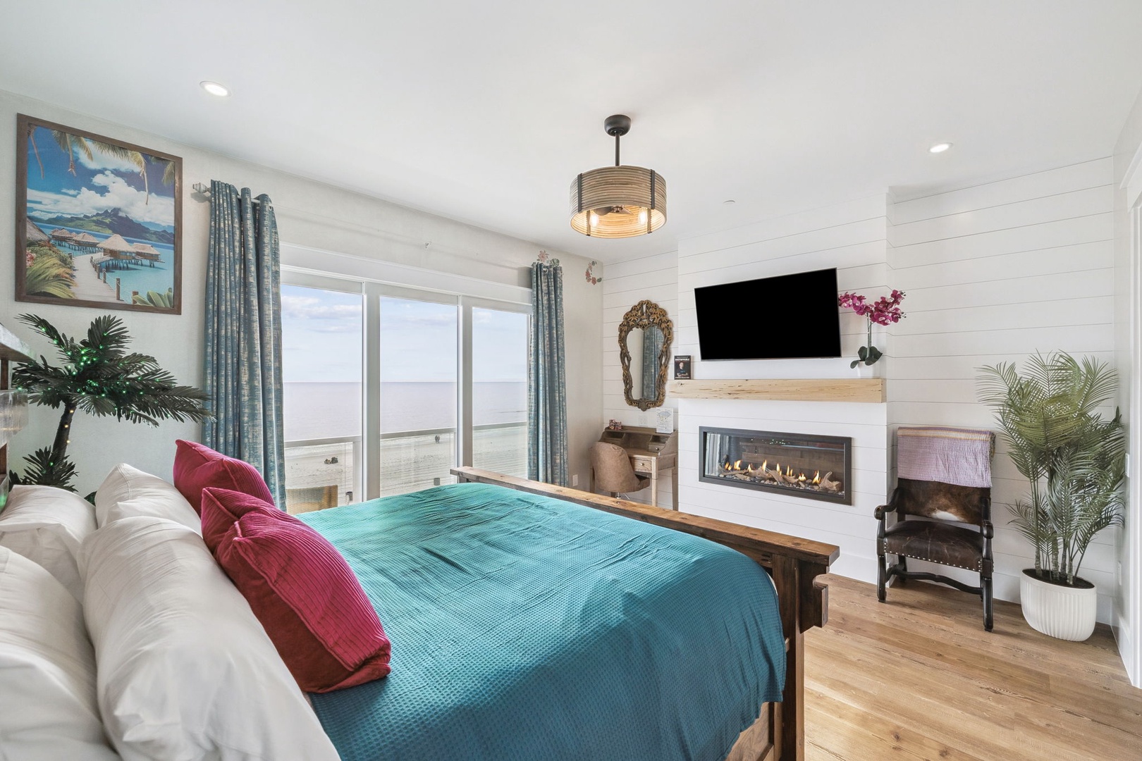 Unwind in your serene bedroom featuring a cozy fireplace, ocean-themed decor, and large windows framing peaceful views.