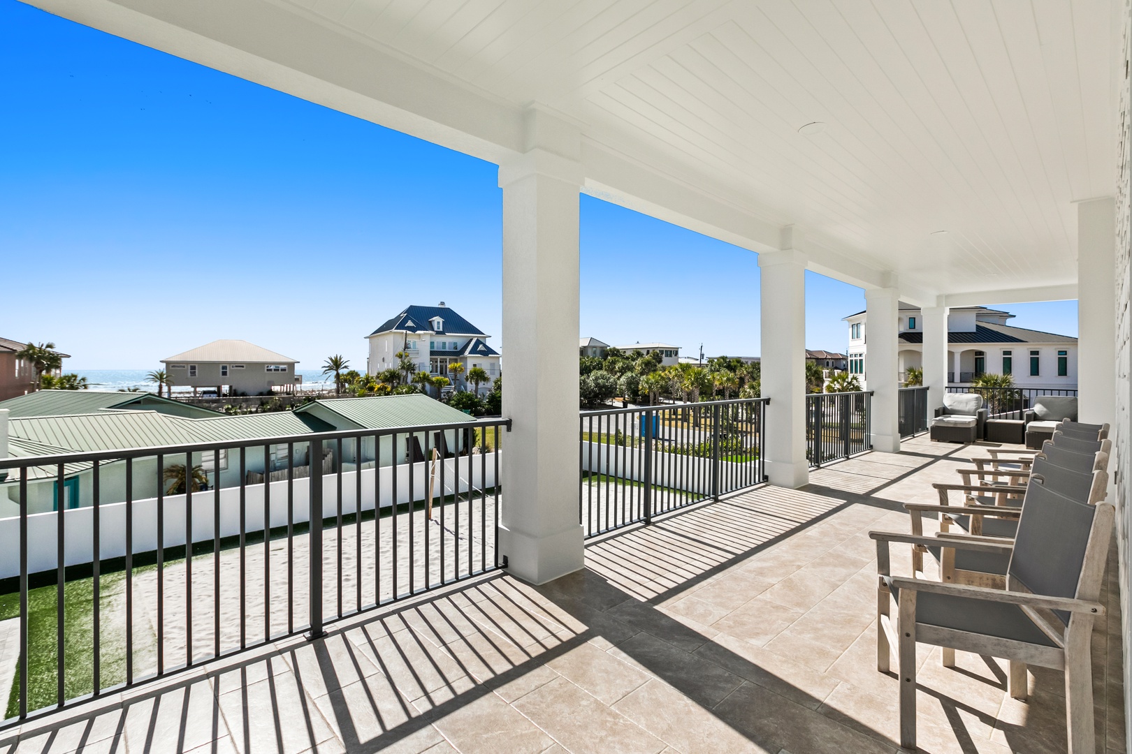 A spacious covered terrace overlooks the surrounding coastal community, with ocean views, palm trees, and nearby homes visible in the distance. Perfect spot for morning coffee or evening relaxation.