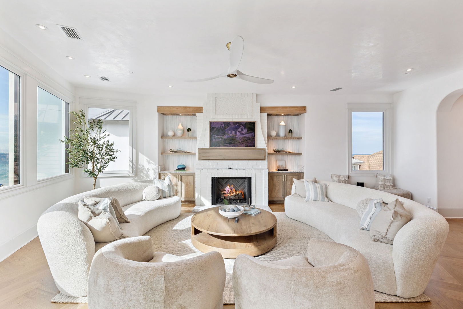 Sink into plush seating in your elegant living room, where natural light pours through panoramic windows, a fireplace adds warmth, and soothing coastal views await.
