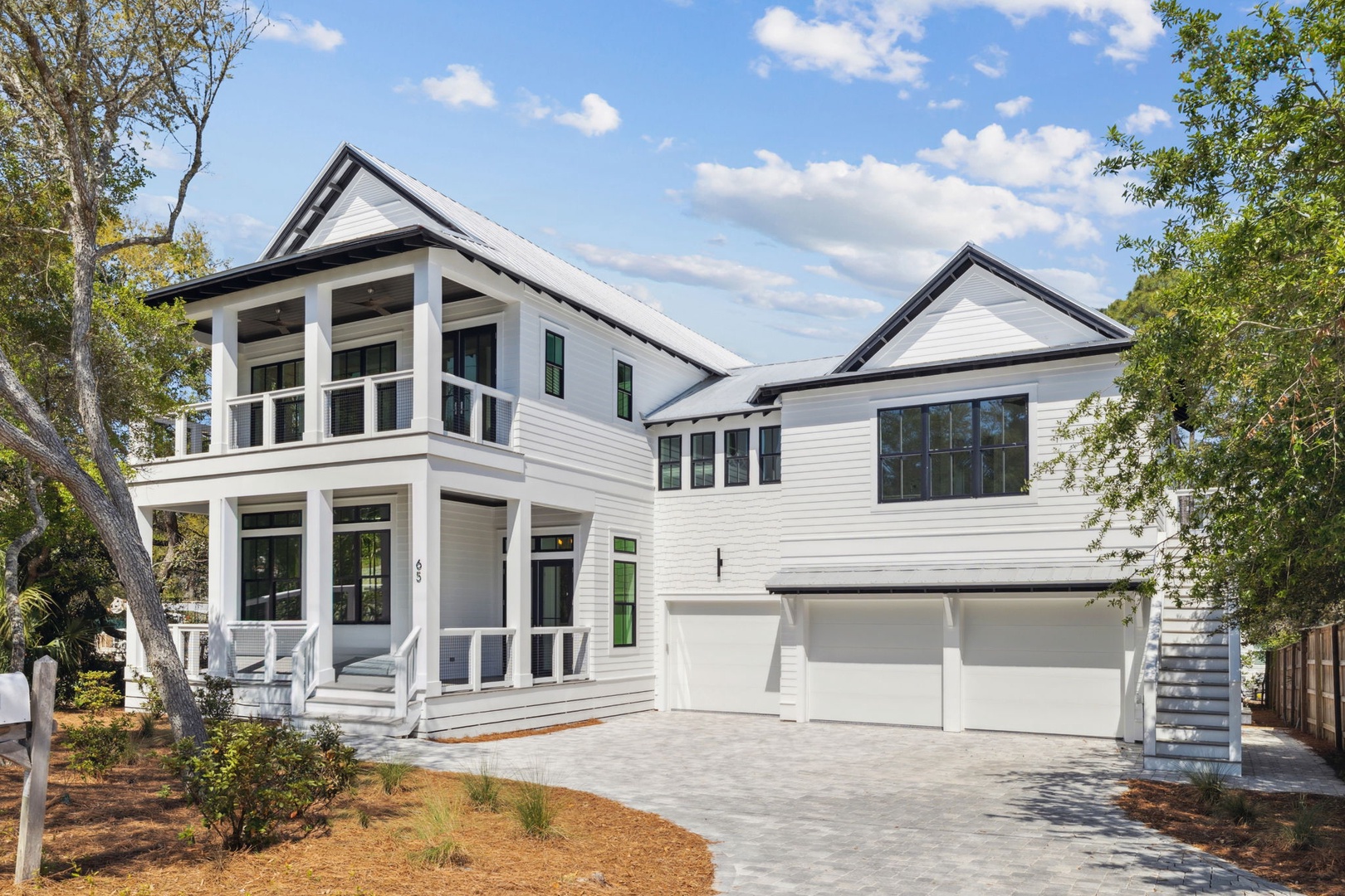 Modern coastal-style home with pristine white siding and spacious garage, nestled among mature trees in a peaceful residential setting.