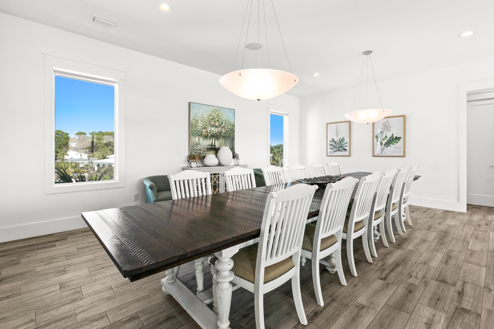 Gather everyone around this spacious dining table, perfectly set for memorable group meals. Natural light pours through windows, highlighting the elegant decor and inviting atmosphere where your vacation stories unfold over shared plates.