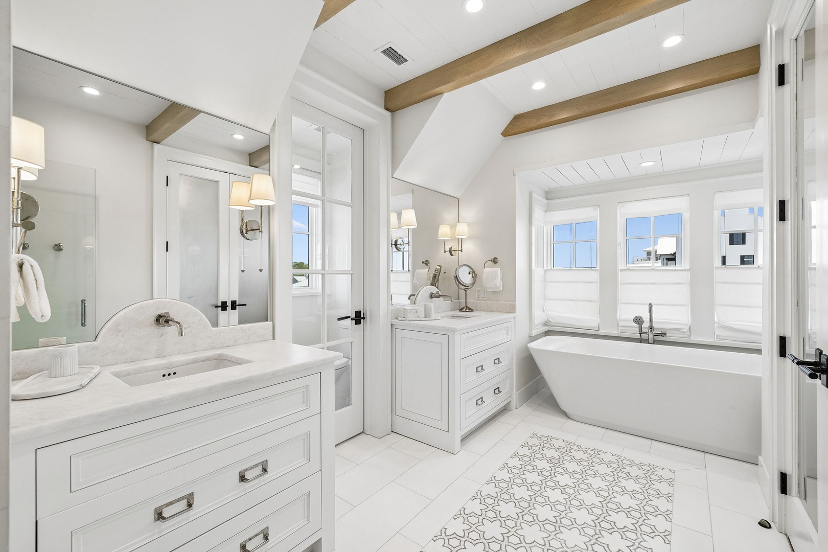 Step into a serene coastal retreat where vaulted ceilings with warm wood beams frame your private sanctuary. Soak in the freestanding tub by sunlit windows or freshen up at elegant dual vanities with soft lighting—your perfect escape.