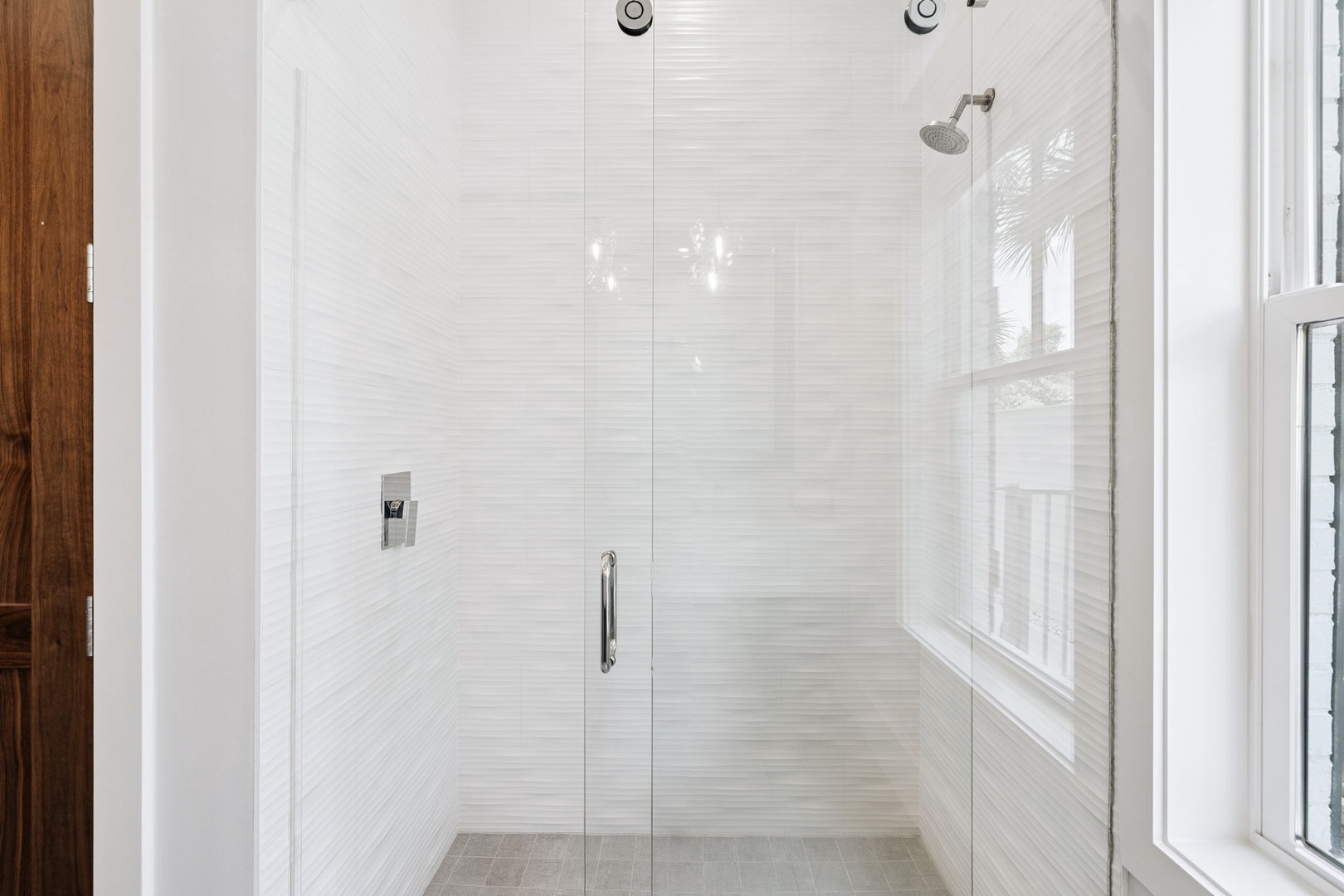 Step into your private glass-enclosed shower with rainfall head, featuring elegant white tiled walls and natural light.
