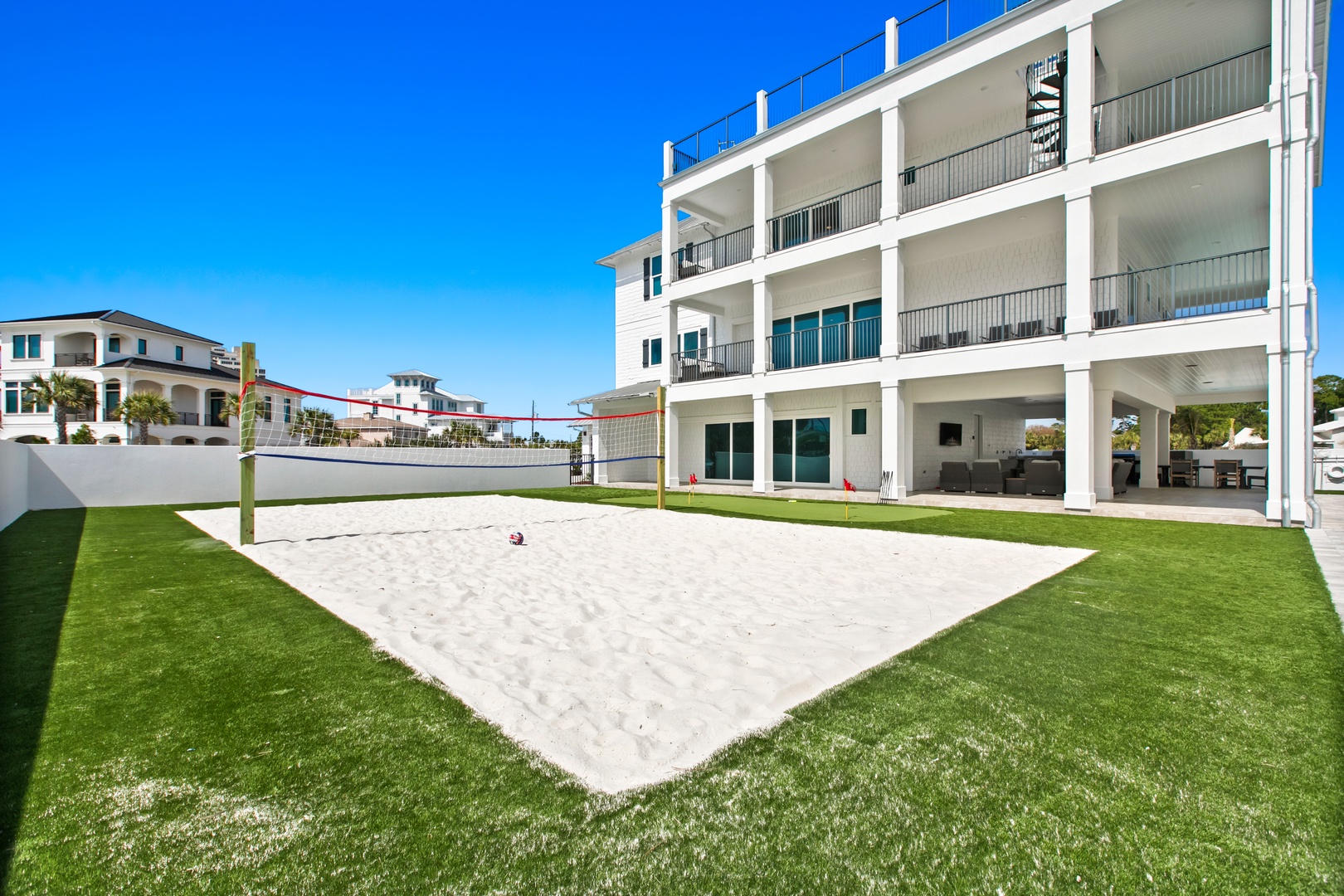 A pristine sand volleyball court surrounded by lush green lawn offers endless recreation and friendly competition. The spacious outdoor area boasts multiple balconies and covered gathering spaces perfect for entertaining.