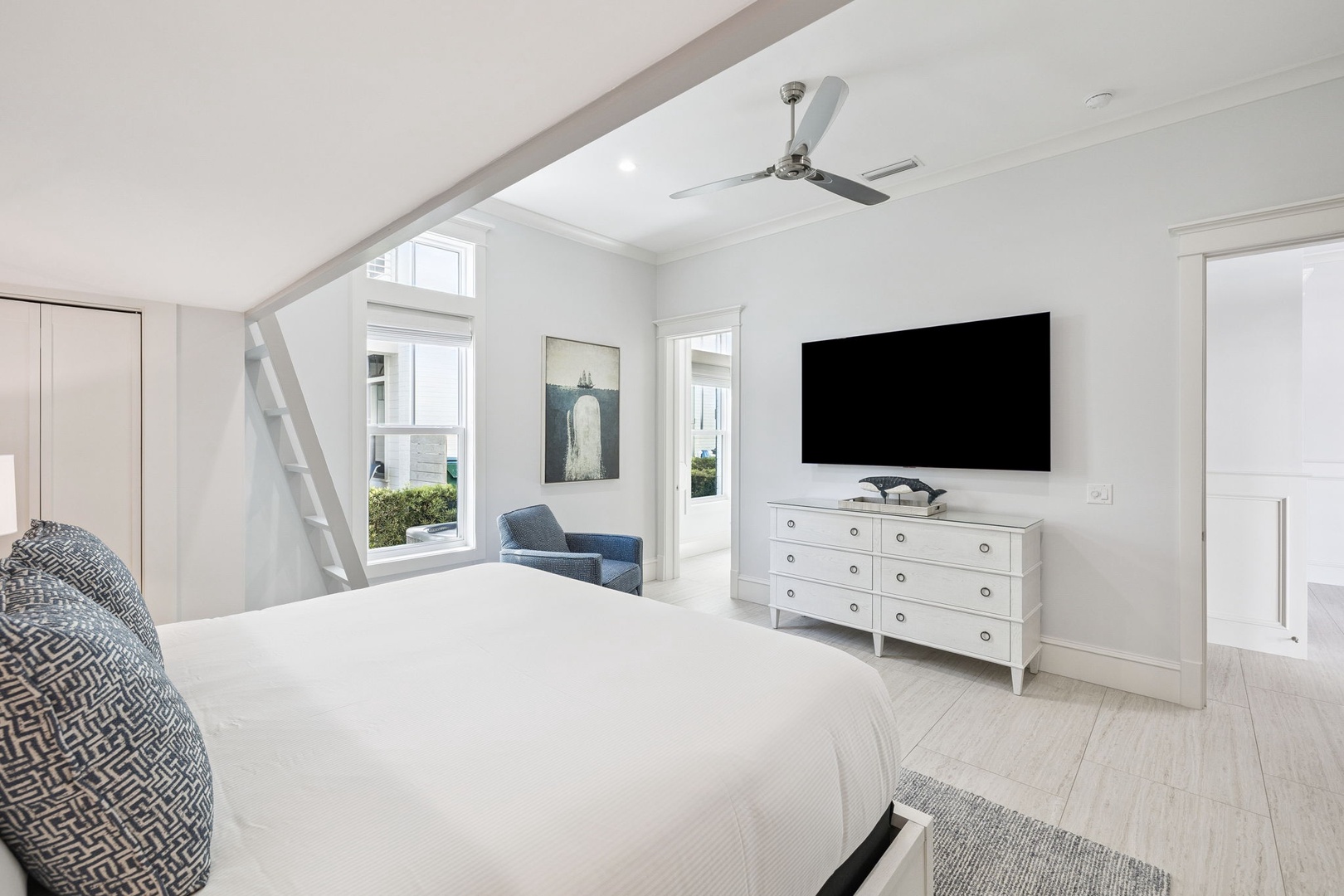 Relax in your bright, airy bedroom featuring a plush king bed, cozy seating nook, and large TV for ultimate comfort.