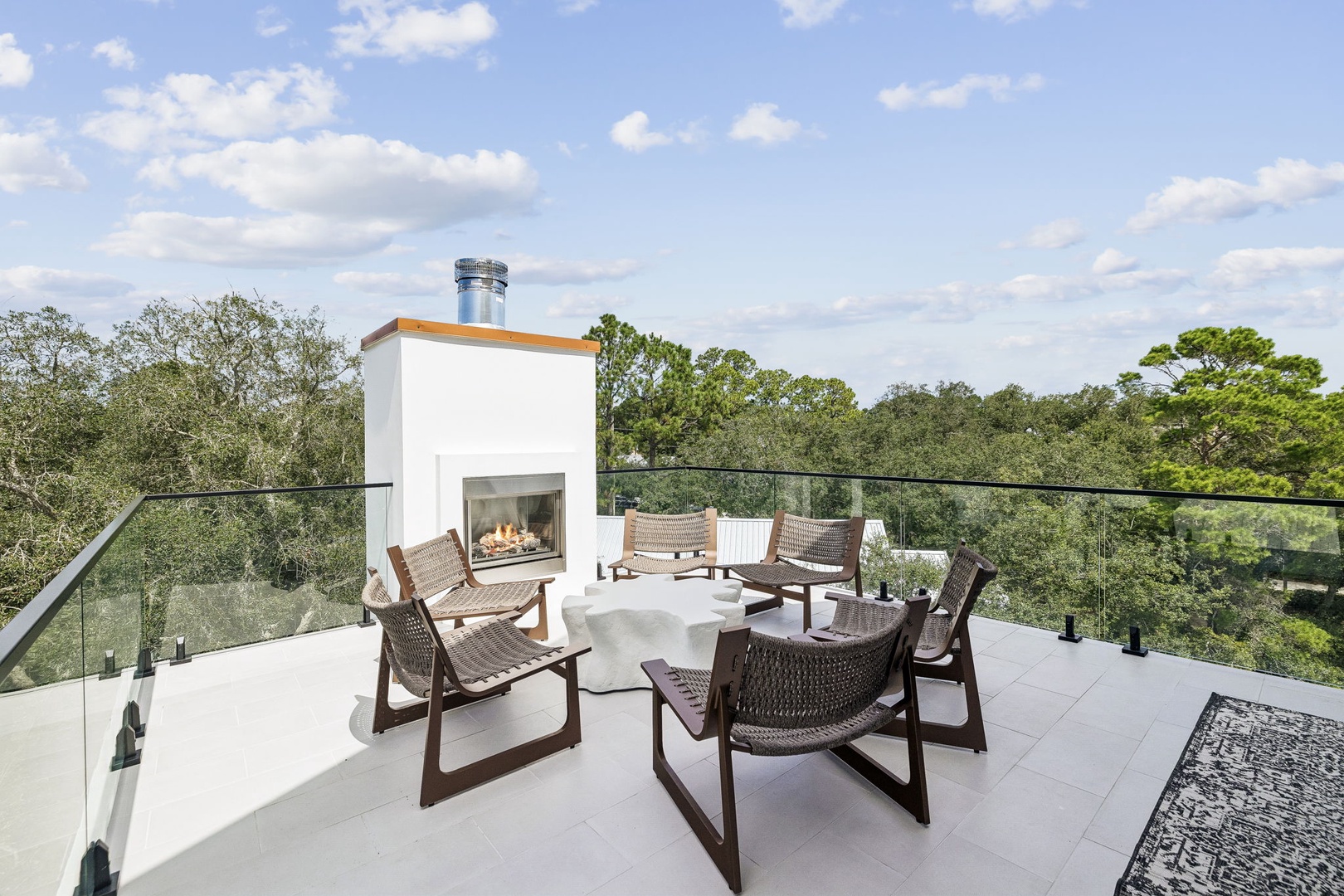An expansive rooftop terrace overlooks lush treetops, featuring a modern outdoor fireplace and stylish woven lounge chairs that create your perfect retreat under the open sky.
