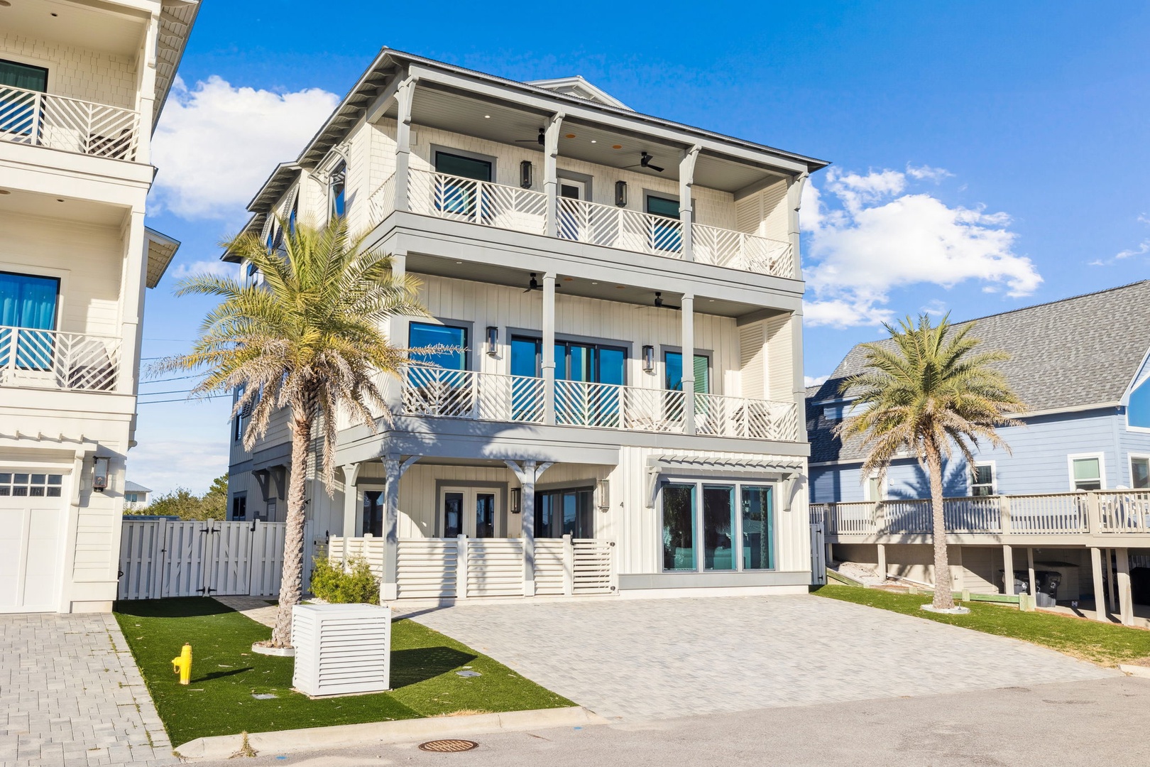 Modern three-story coastal home with palm trees and distinctive blue accents in a sunny beachside neighborhood.