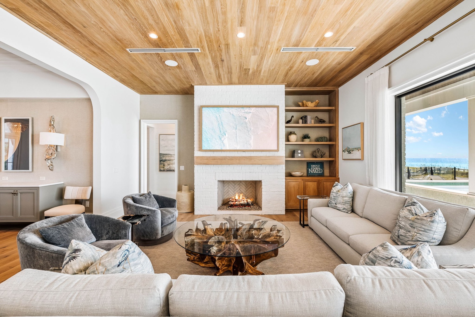 Sink into plush seating beneath stunning wood-planked ceilings as your fireplace glows warmly and natural light floods through sliding glass doors, creating your perfect retreat for relaxation or lively conversation.