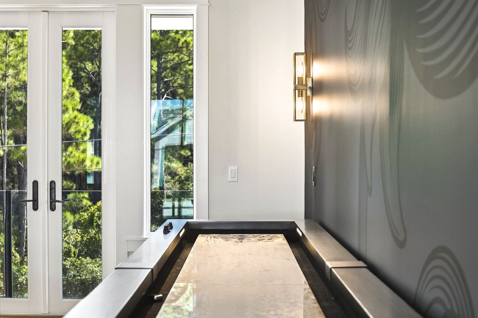 Step into this bright, stylish space where modern design meets natural light. The elegant wall sconce and warm textures frame your entry, while glass doors reveal a tranquil, tree-filled escape just outside.