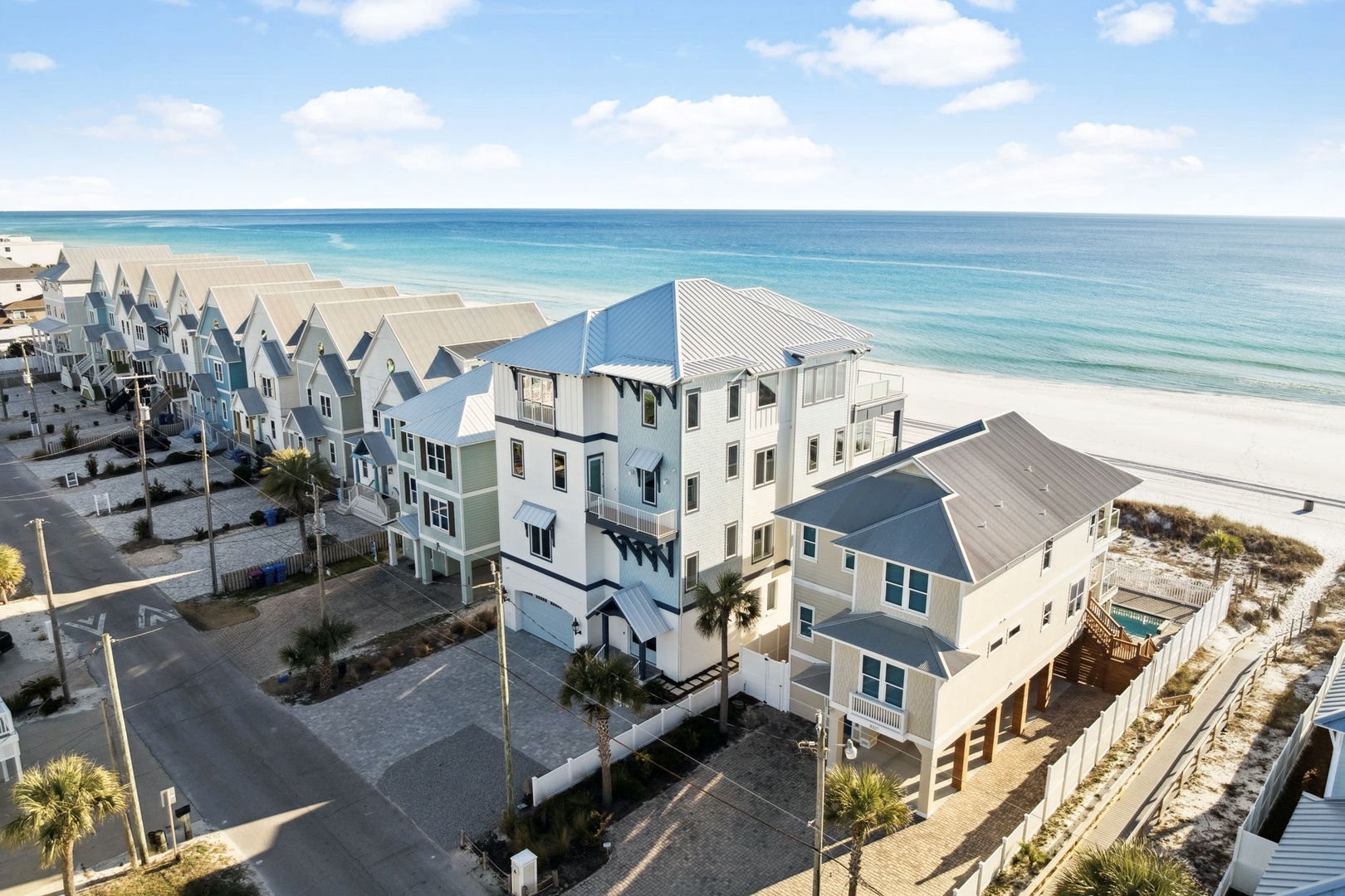 Aerial view of beachfront vacation homes along pristine white sand and crystal-clear waters in a coastal community.