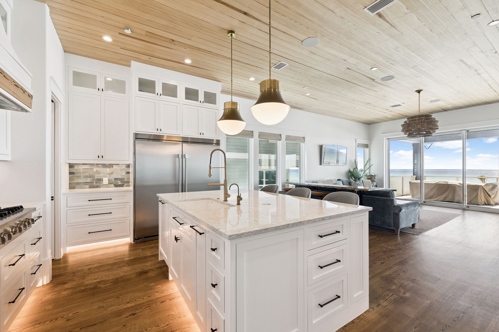 Your gourmet kitchen features marble counters, stainless appliances, and pendant lighting, flowing seamlessly into the living space with ocean views.