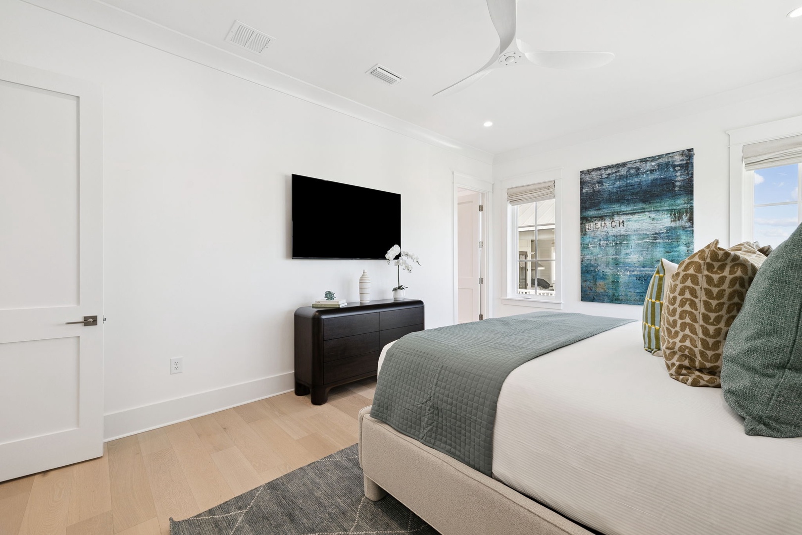Drift off in this serene bedroom featuring a plush bed, calming coastal artwork, and modern entertainment for your perfect retreat.