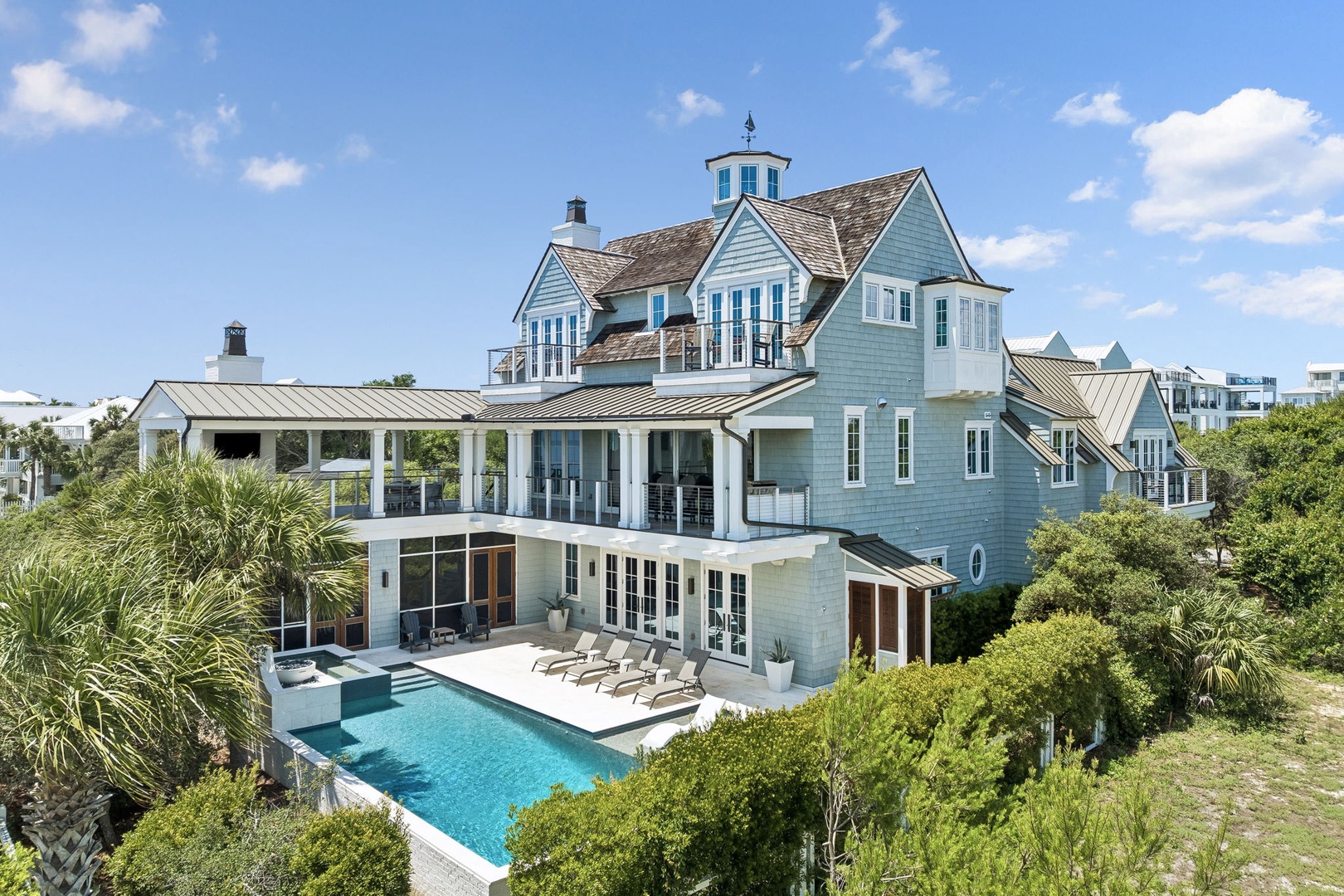 A stunning coastal estate featuring classic architecture with a turret, wraparound balconies, and a private pool nestled among lush tropical greenery—perfect seaside living.