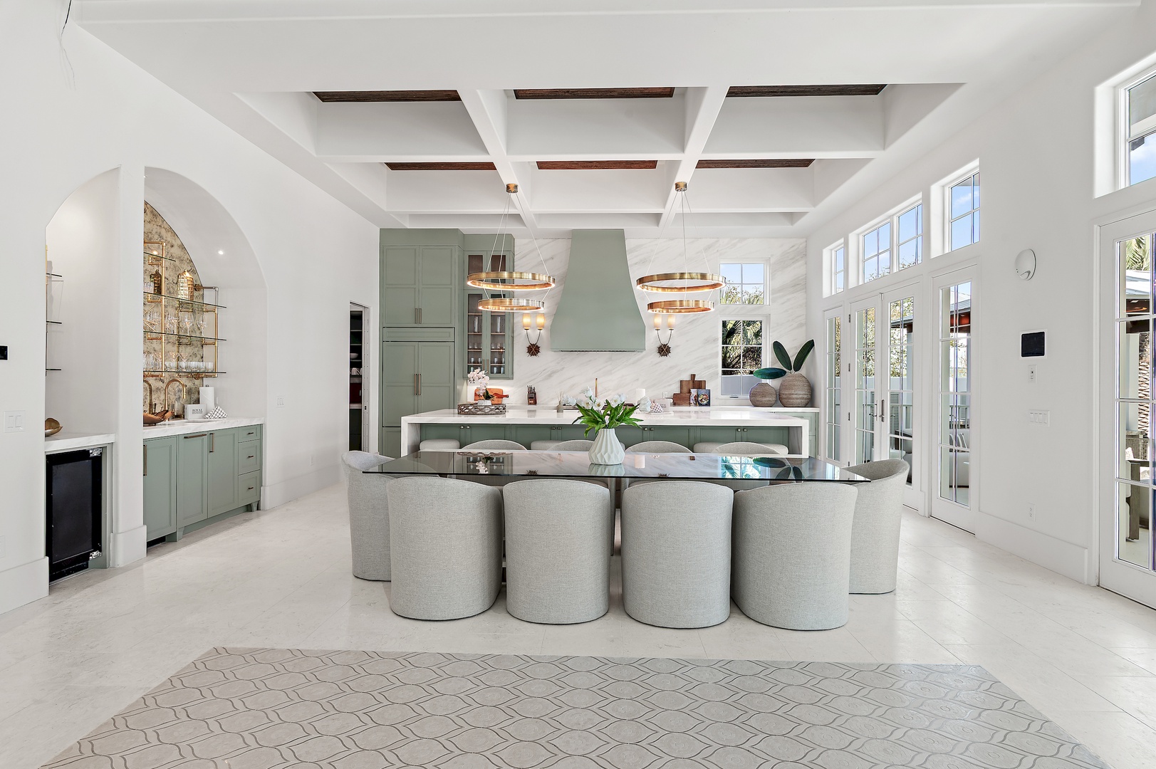 Step into an elegant open-concept kitchen and dining space where soft sage cabinetry, soaring ceilings, and abundant natural light create a serene culinary haven for your getaway.