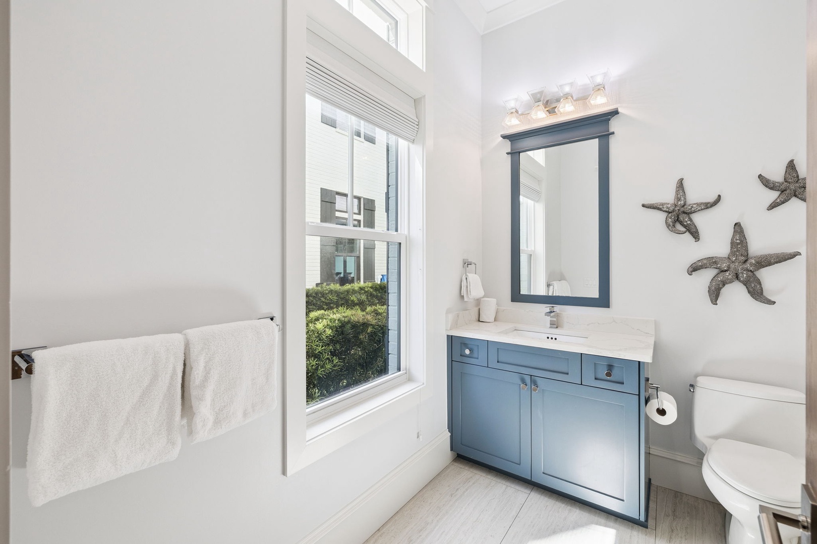 Refresh in your charming coastal bathroom with blue vanity, nautical starfish decor, and soft white towels awaiting your arrival.