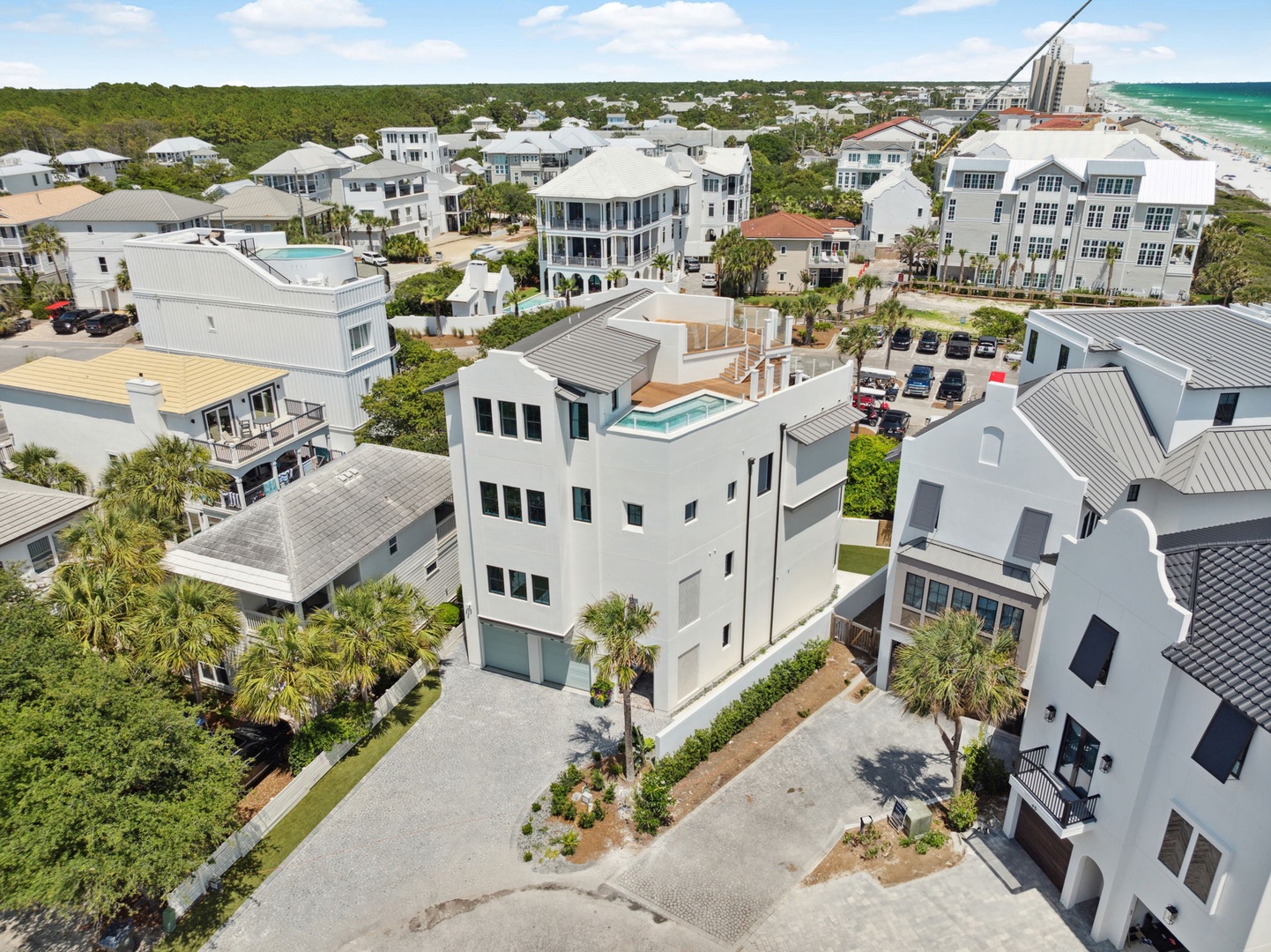 Aerial view of a modern coastal property nestled among elegant vacation homes, with the beach and turquoise Gulf waters visible in the distance.