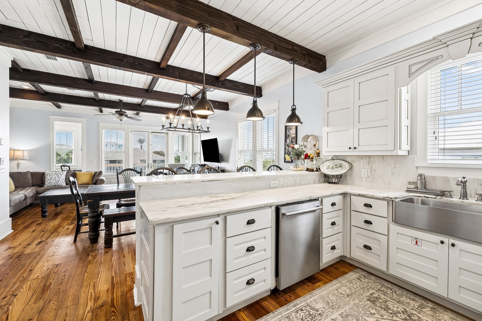 Chef's kitchen with soaring wood beams, marble countertops, and welcoming island. Sunlight streams through shuttered windows, illuminating rich hardwood floors and flowing into the open living space.