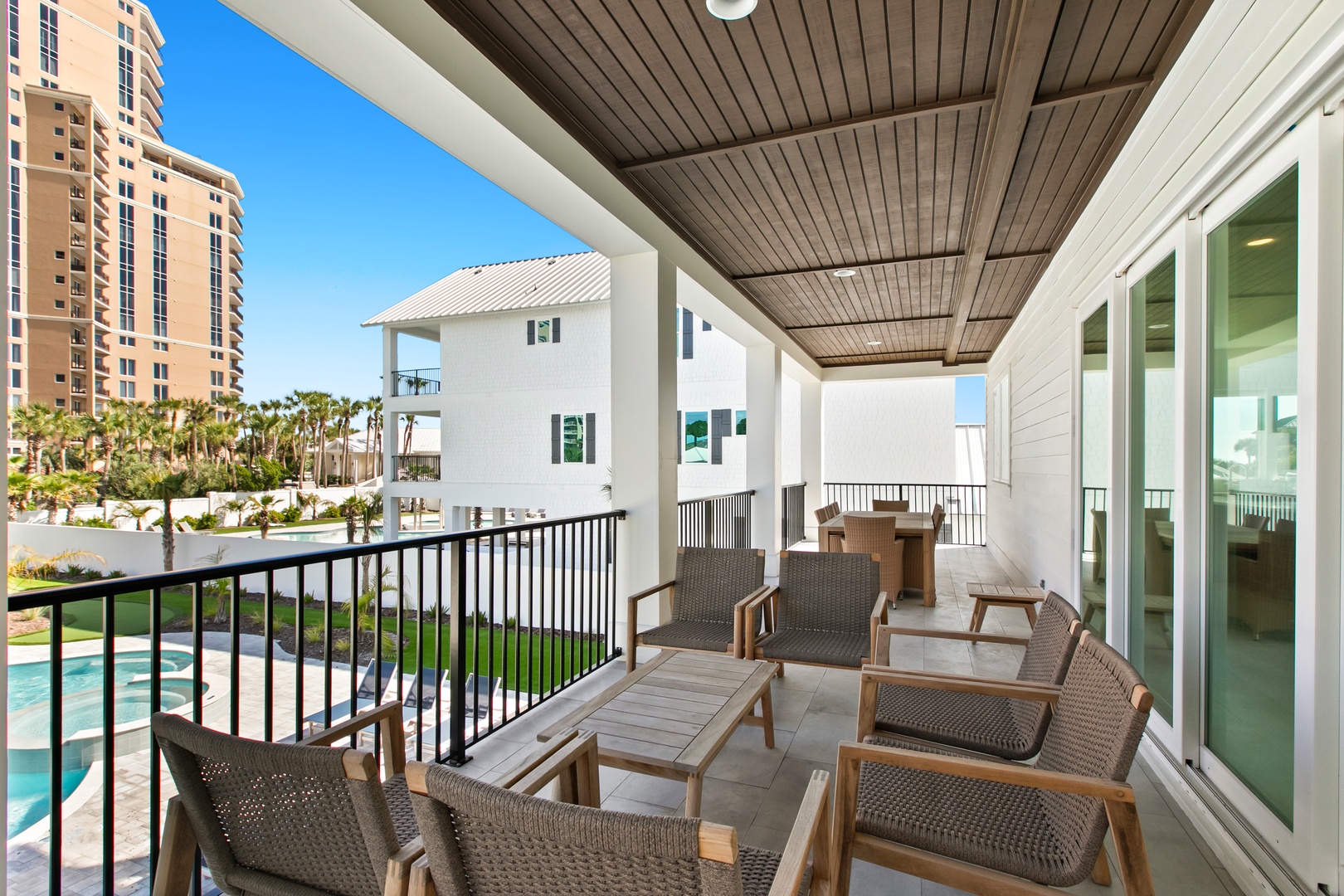 A covered balcony with stylish outdoor seating overlooks a tropical landscape. A tranquil view of surrounding properties and lush palms creates a peaceful setting to relax in your own private retreat.