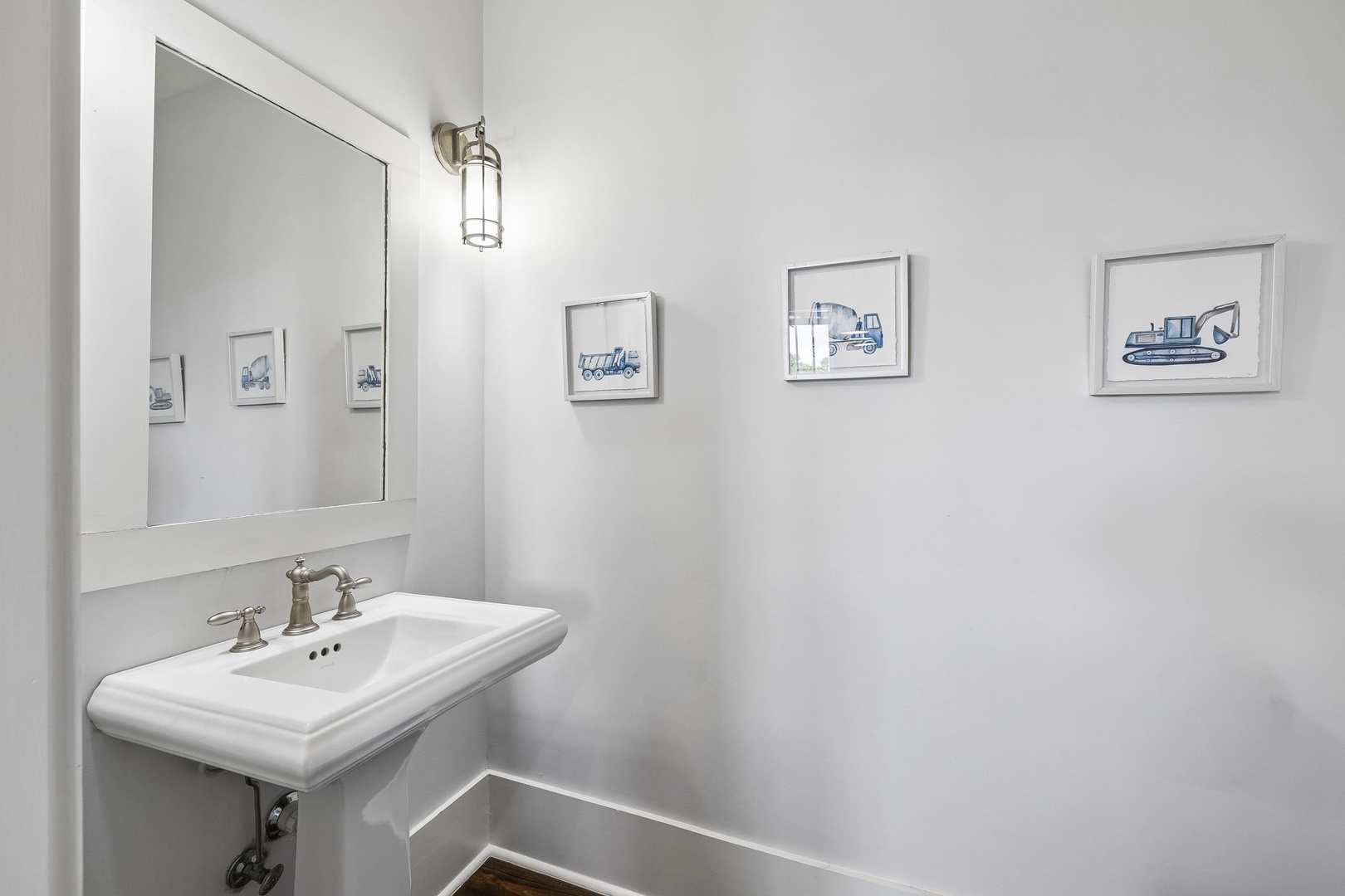 This bright bathroom features a classic pedestal sink with vintage-style fixtures and charming construction truck art that adds a playful touch to your space.