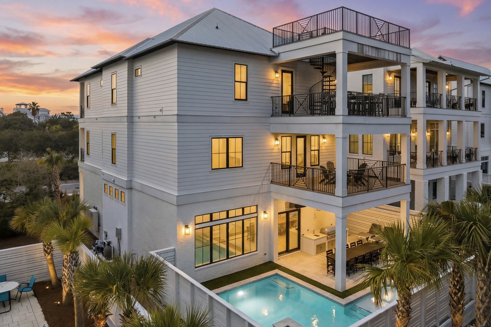 Stunning three-story coastal home with private pool and multiple balconies, surrounded by swaying palms under a painted sunset sky.