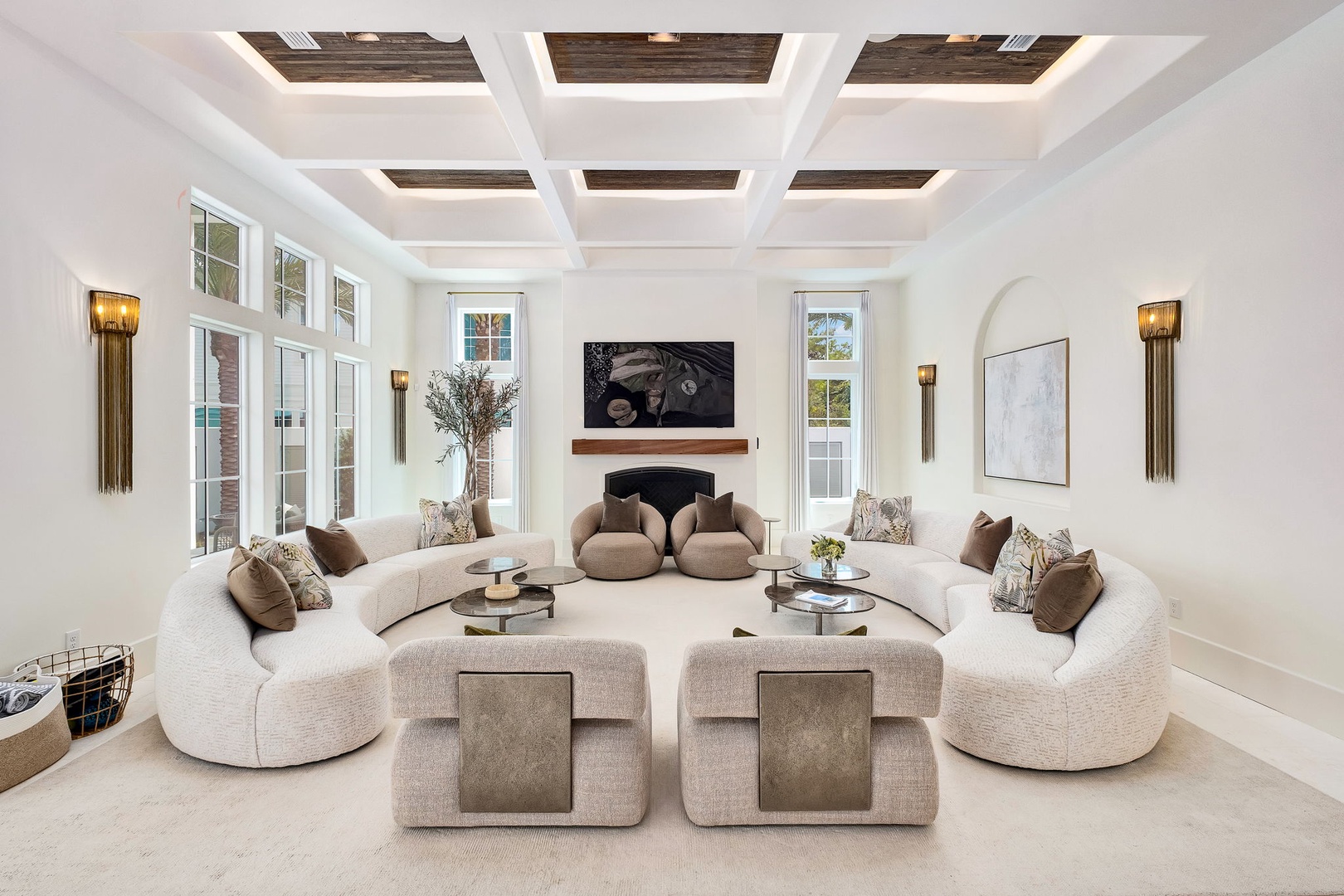 Unwind in your spacious living room where natural light pours through elegant windows, plush curved seating invites conversation, and a stunning coffered ceiling with wood accents creates an atmosphere of refined comfort.