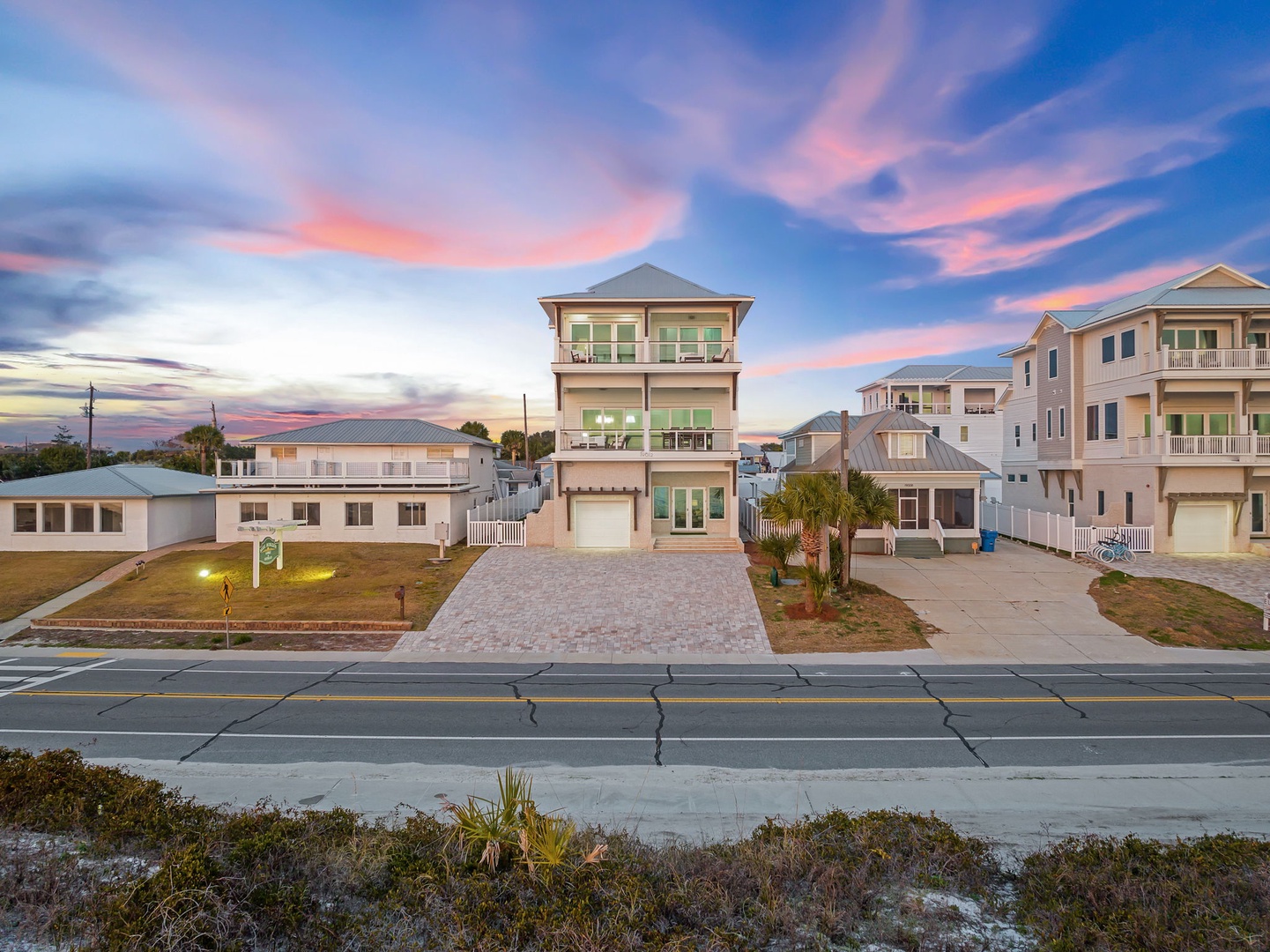 Stunning three-story beach house with dramatic sunset skies painting the coastal neighborhood in vibrant colors.
