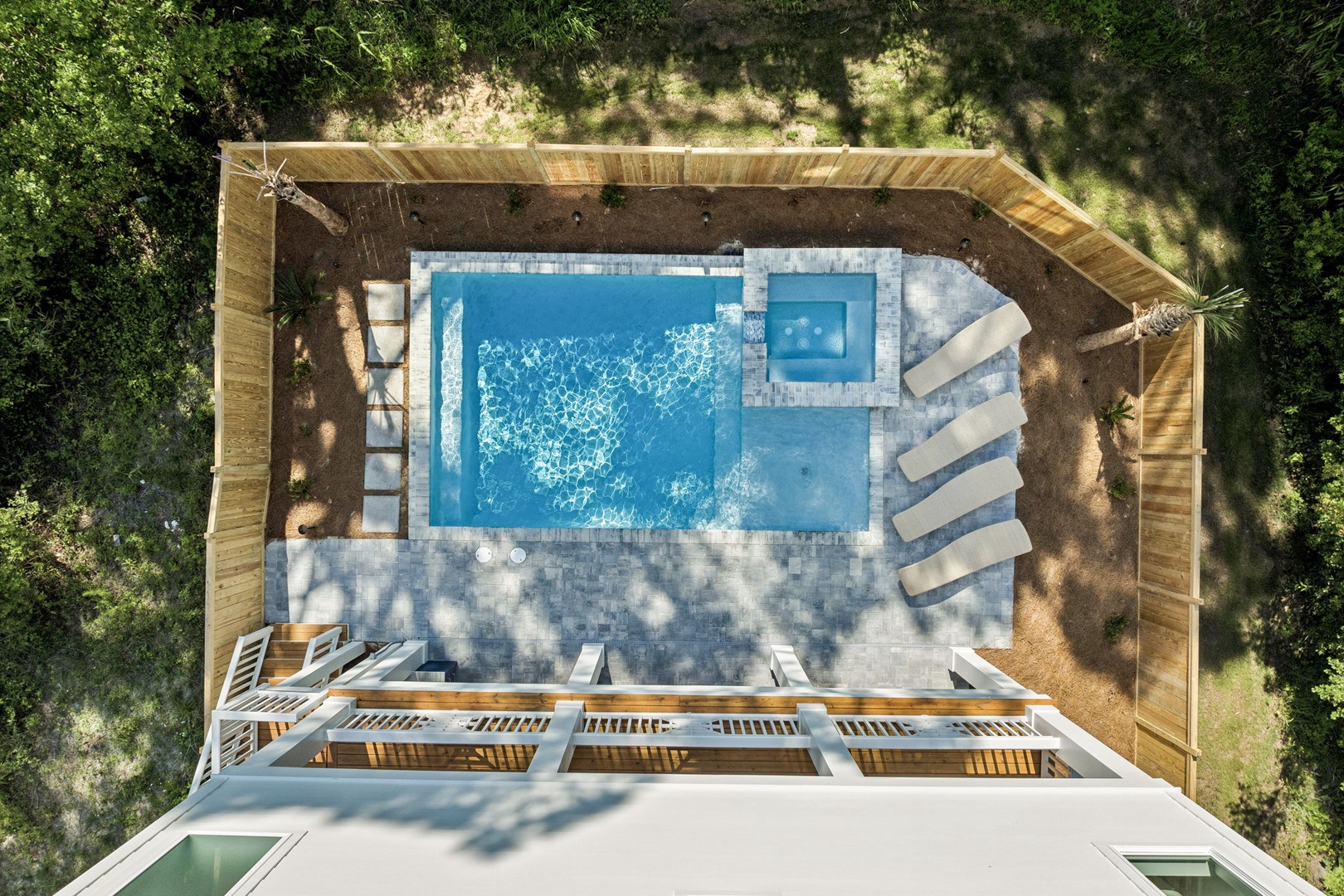 Aerial view of the property featuring an inviting swimming pool, hot tub, and sunbathing area surrounded by lush greenery and natural landscaping.