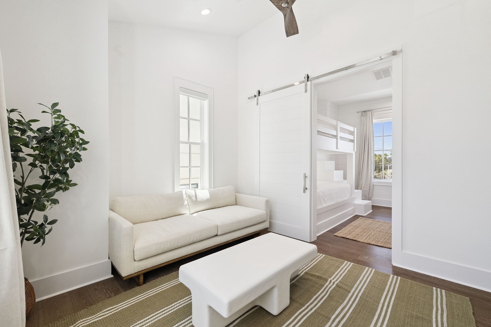 Relax in your bright, airy living space with soft seating and natural light streaming through tall windows.