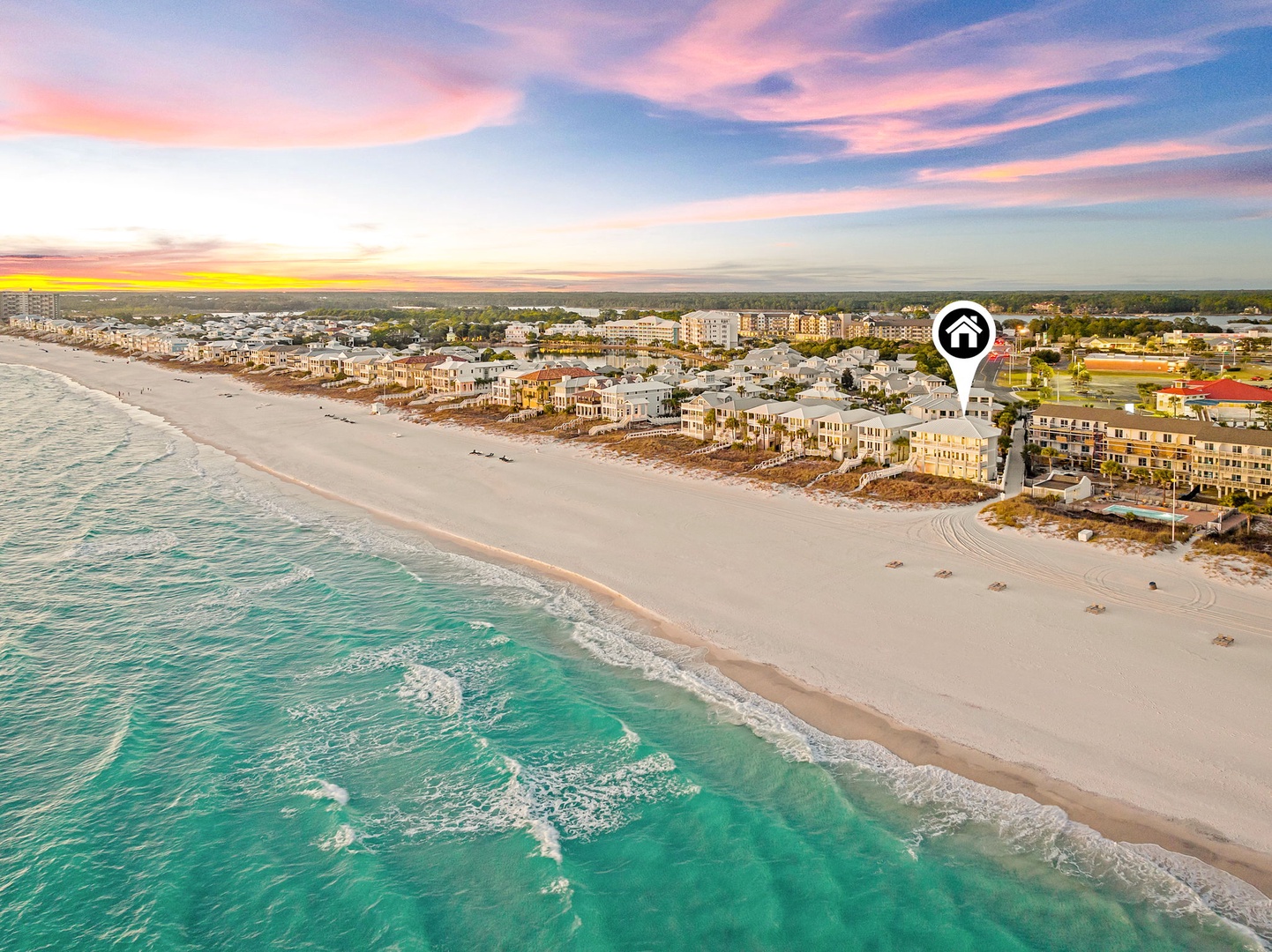 Aerial view of the beachfront property located along pristine white sand and turquoise Gulf waters, with nearby coastal neighborhoods and easy beach access at sunset.