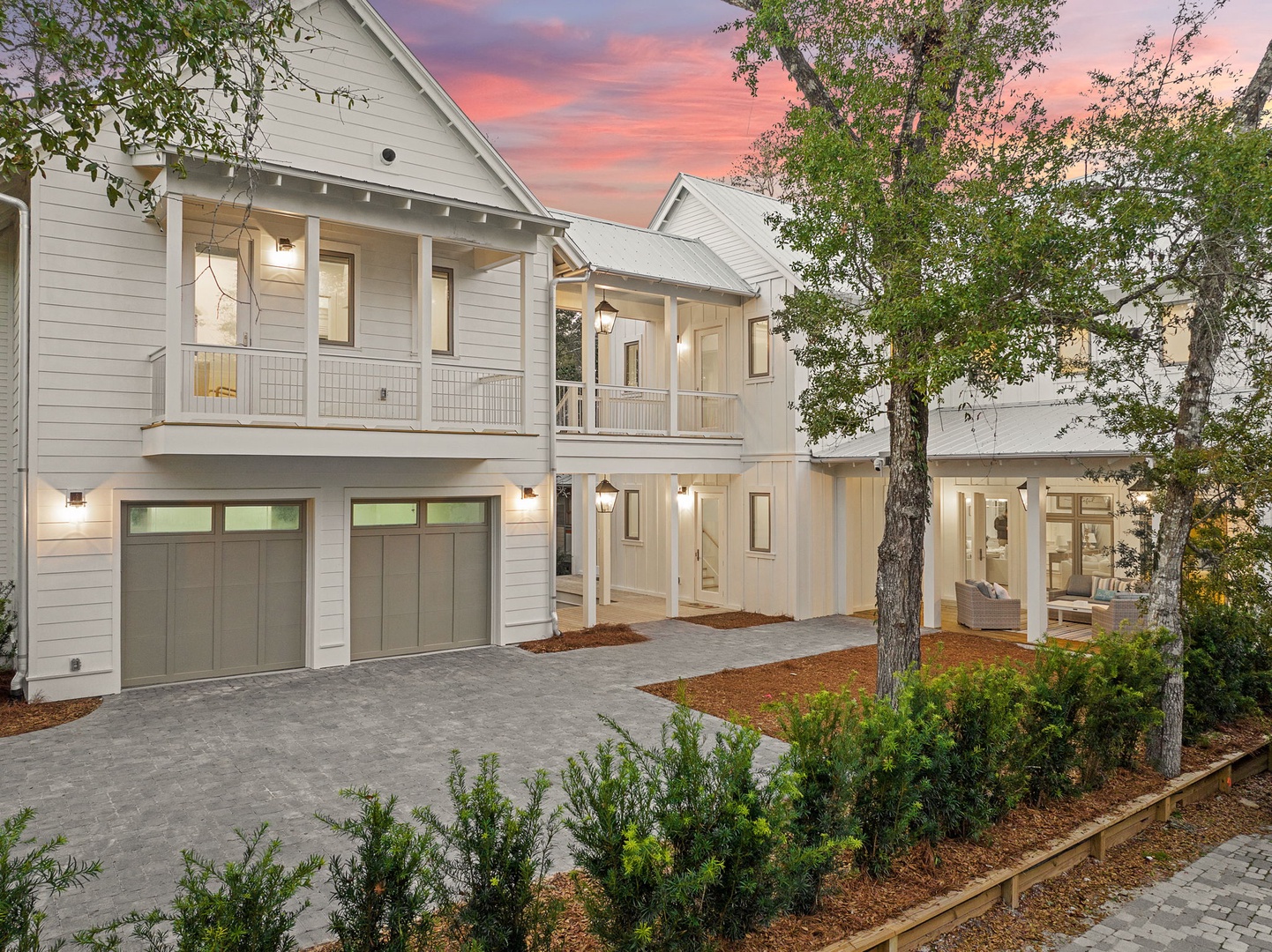 Charming white coastal home with inviting front porches and elegant string lights under a stunning sunset sky.