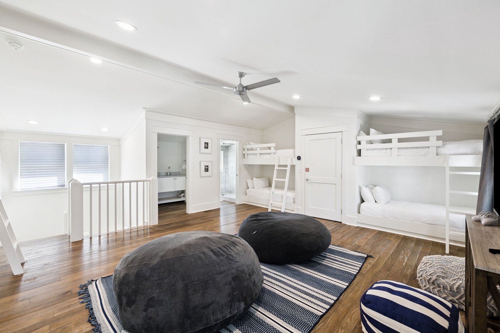 Gather with family in this spacious bunk room featuring pristine white beds, cozy floor cushions, and warm hardwood floors perfect for kids' adventures.