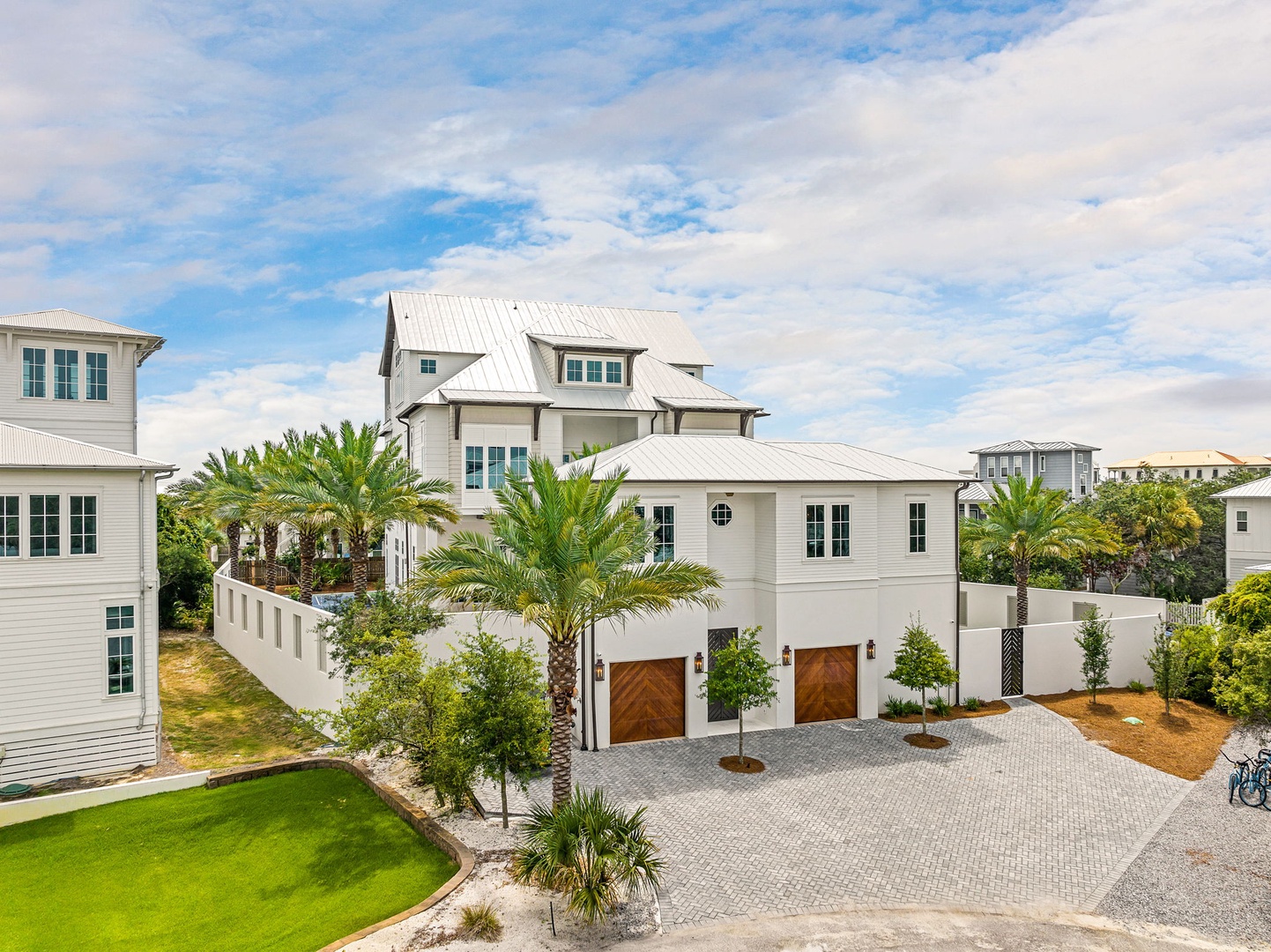 A pristine white coastal retreat nestled among palm trees, featuring classic metal roofing and elegant architectural details set within a serene beachside community.