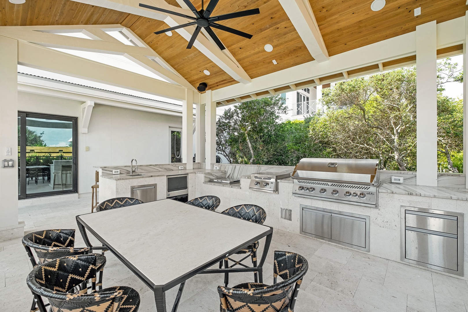 Your private outdoor kitchen awaits with a built-in grill, elegant countertops, and covered dining beneath a vaulted wood ceiling—perfect for alfresco gatherings surrounded by lush greenery.