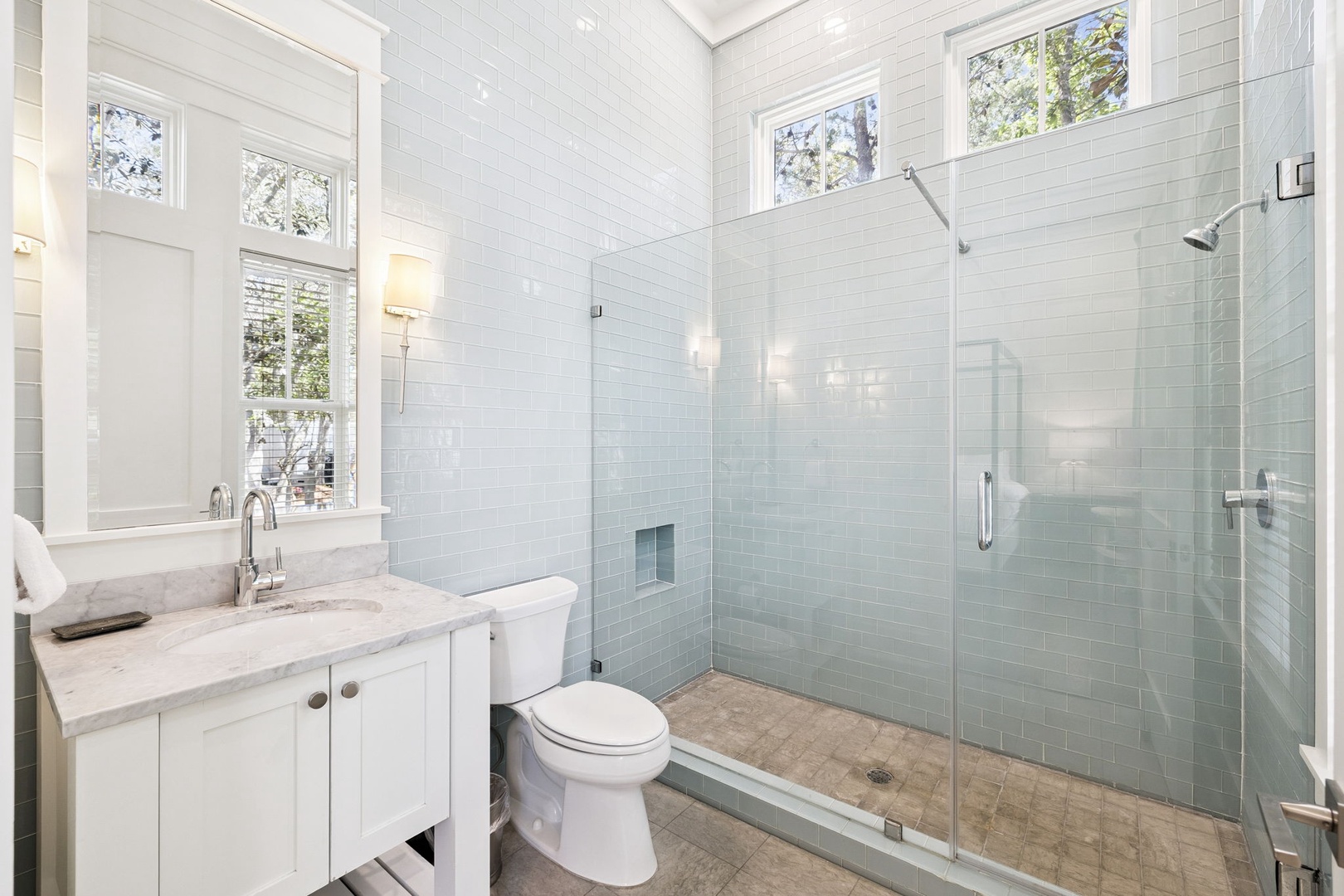 Refresh in your spa-like bathroom with a spacious glass shower, elegant marble vanity, and natural light streaming through multiple windows.