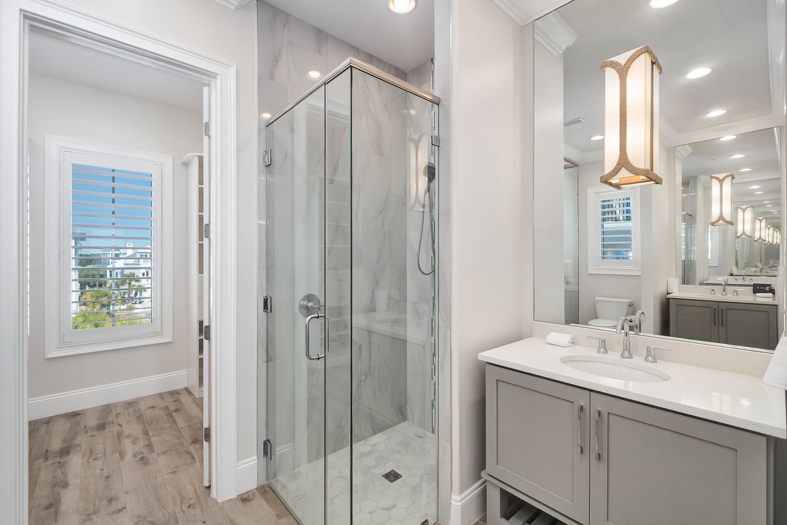 Step into your spa-like marble bathroom featuring a glass-enclosed rain shower and elegant dual vanities under warm designer lighting.