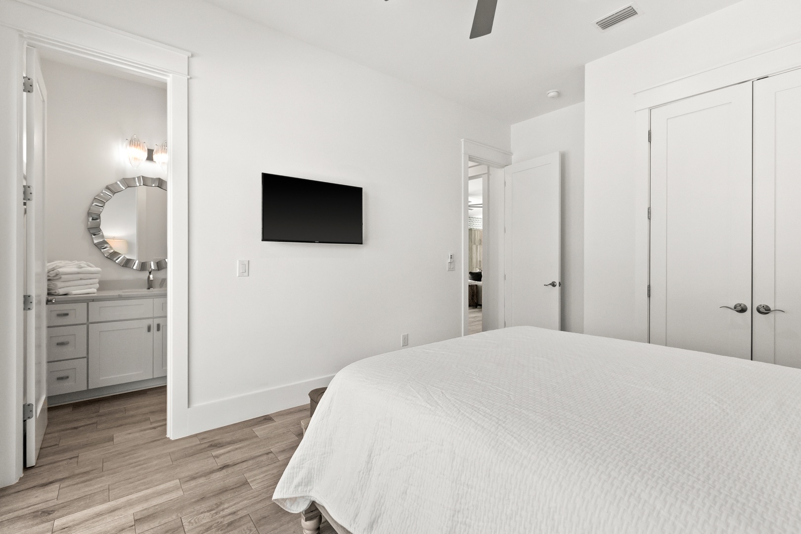 Your serene bedroom retreat features a plush bed and warm wood floors, with a bright ensuite bathroom just steps away through the adjoining doorway.