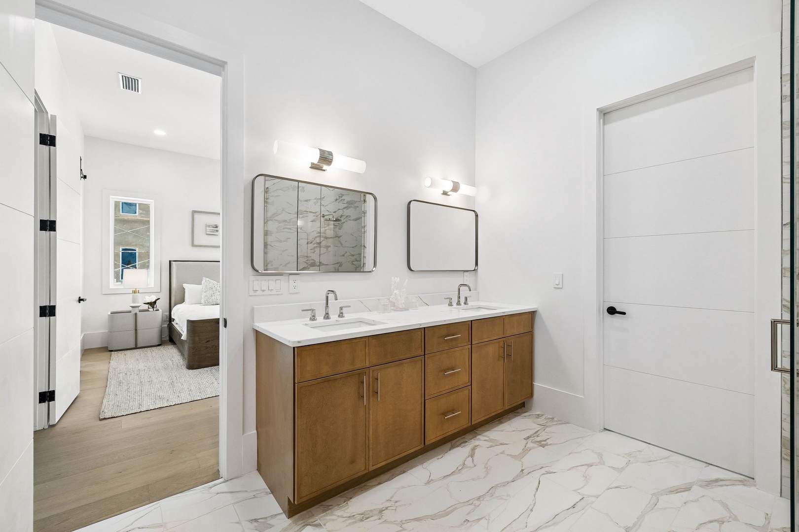 Step into your elegant dual-vanity bathroom with warm wood tones and marble details. The bright space opens to your private bedroom, creating a seamless retreat for relaxation.