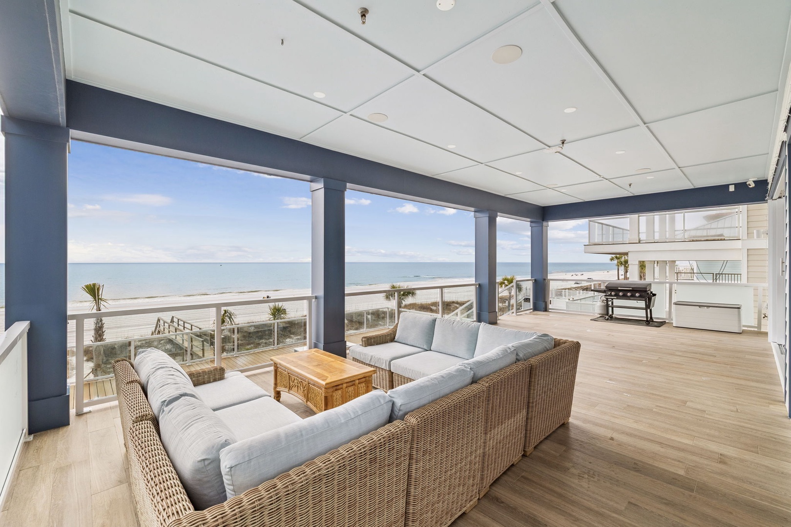 Unwind in your spacious oceanfront living area where floor-to-ceiling windows frame endless sea views and comfortable wicker seating invites relaxation.