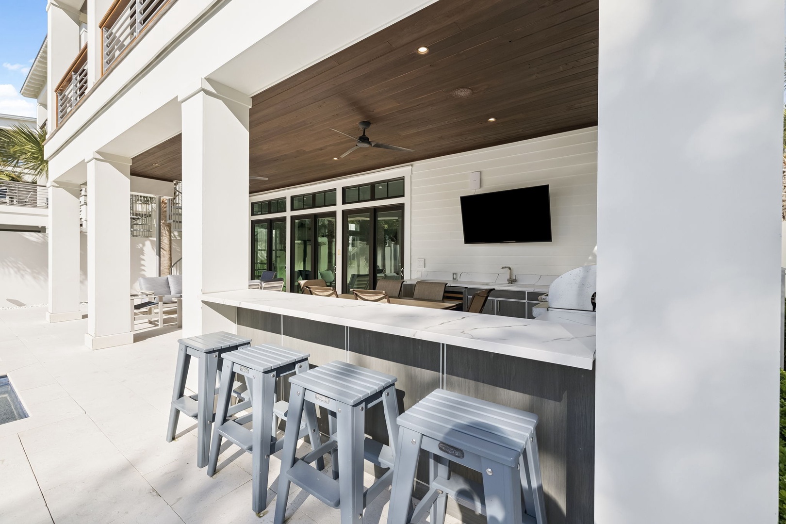 Your outdoor kitchen becomes the heart of entertaining, featuring marble countertops, modern appliances, and bar seating for memorable gatherings.