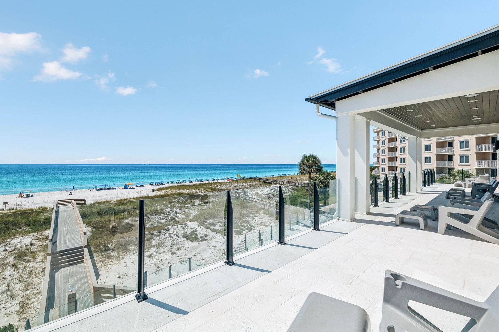 Stunning beachfront terrace with glass railings and lounge chairs, featuring direct beach access and crystal-clear turquoise waters just steps from your door.