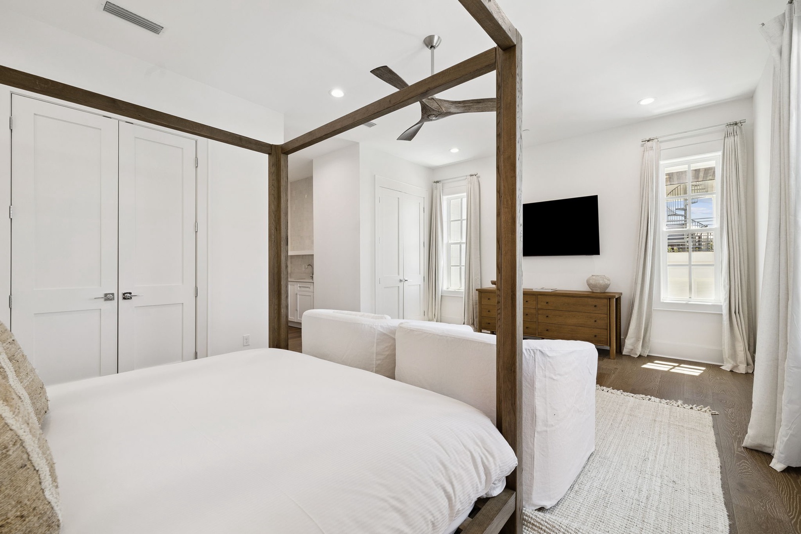 Your spacious bedroom offers crisp white linens on a stunning canopy bed, with natural light streaming through tall windows.