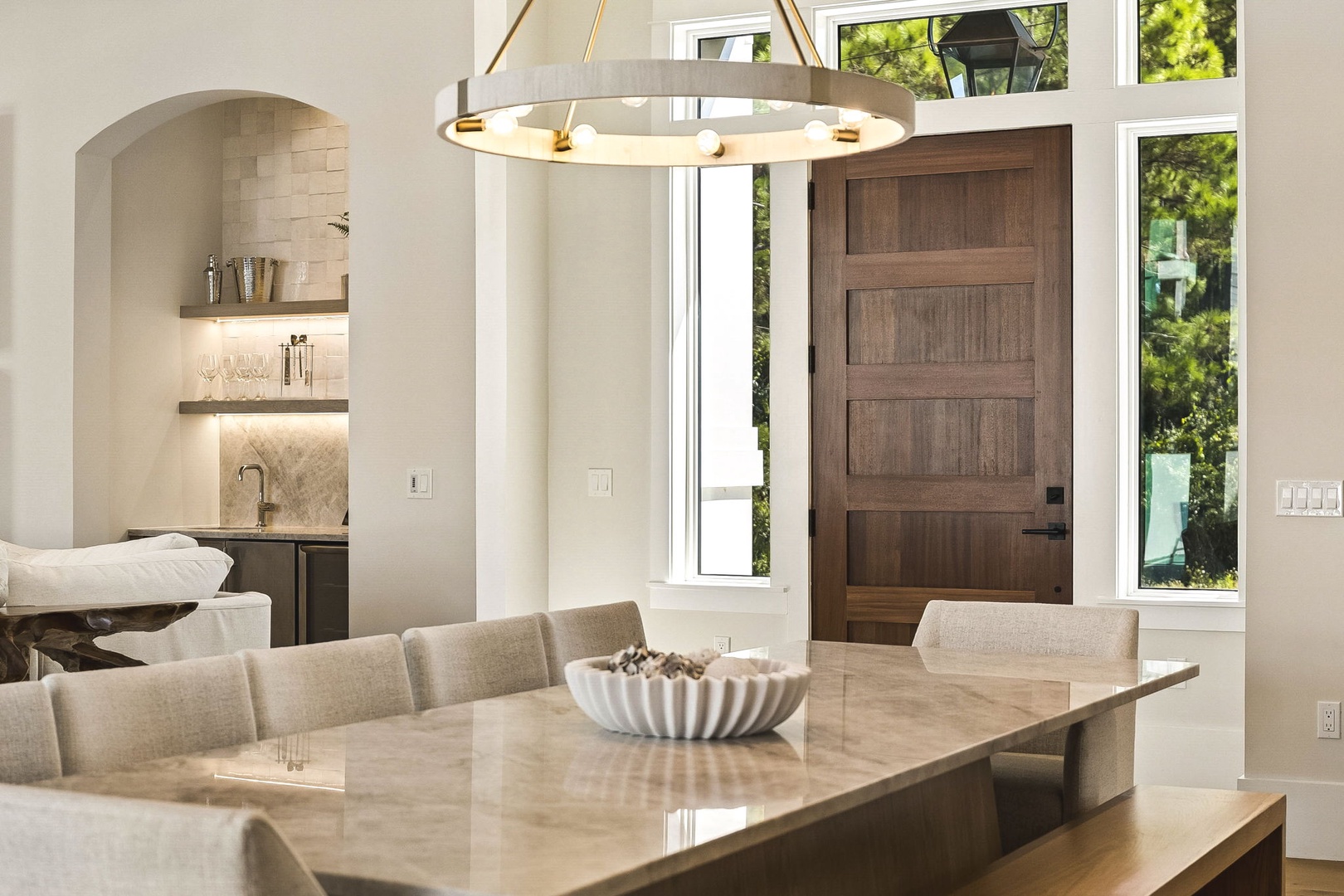 Step into your elegant dining space, where a stunning circular chandelier illuminates your gatherings. Natural light floods in through tall windows flanking the handsome wooden door, while the open layout connects you to your wet bar retreat.