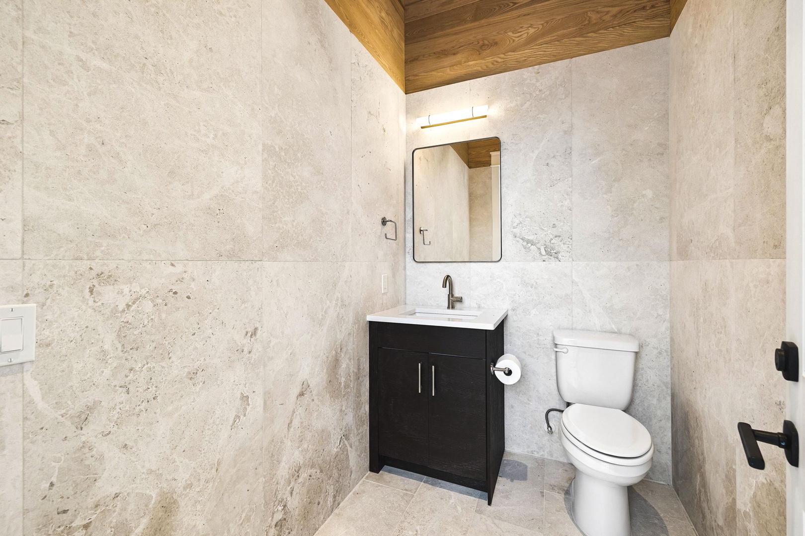 Your private bathroom combines rustic warmth with modern comfort, featuring a sleek vanity, clean lines, and textured stone walls beneath a warm wood ceiling.