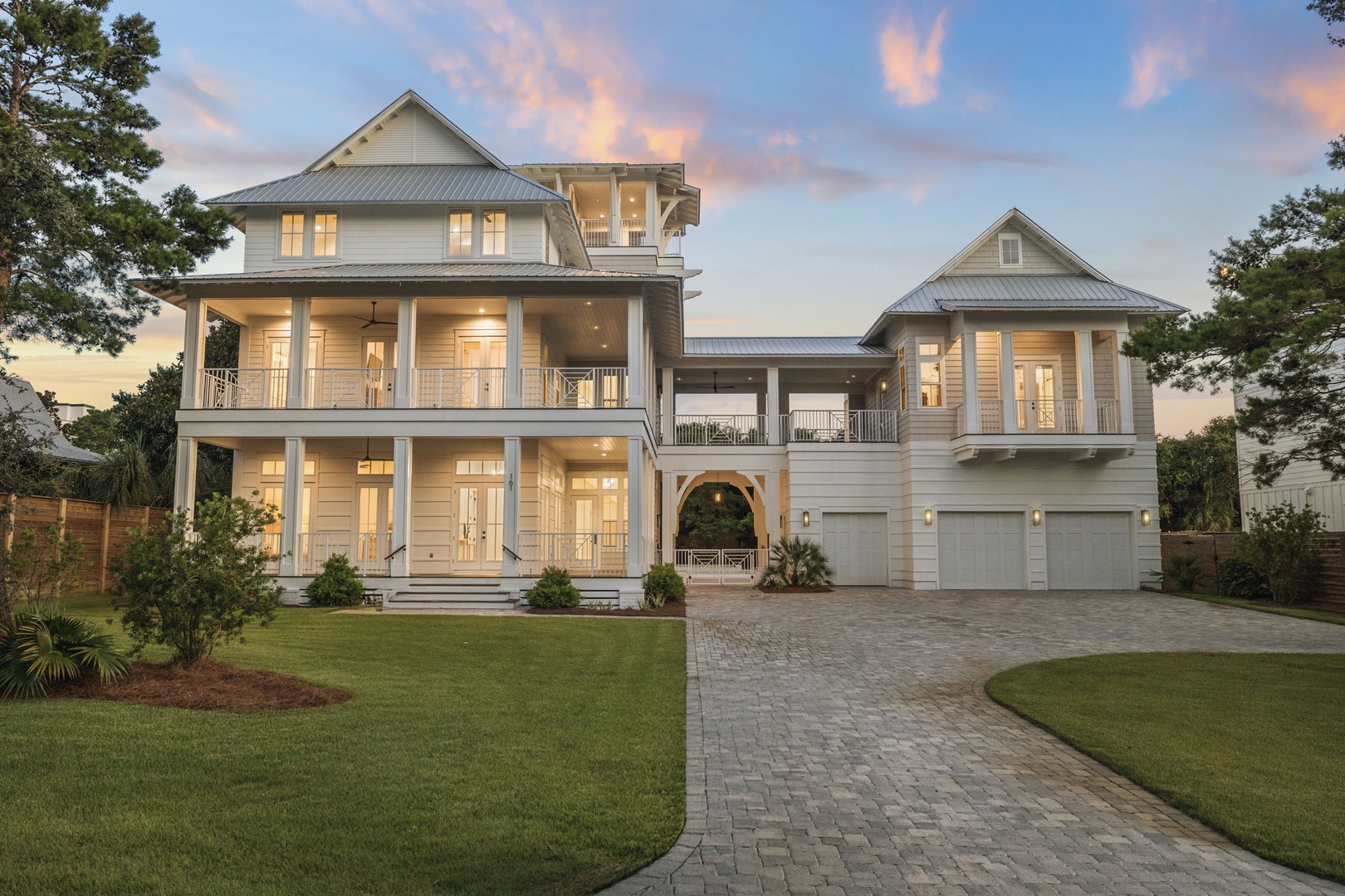 An elegant coastal-style property featuring classic architecture with multiple porches and balconies, surrounded by landscaped grounds and mature trees in a peaceful residential setting.