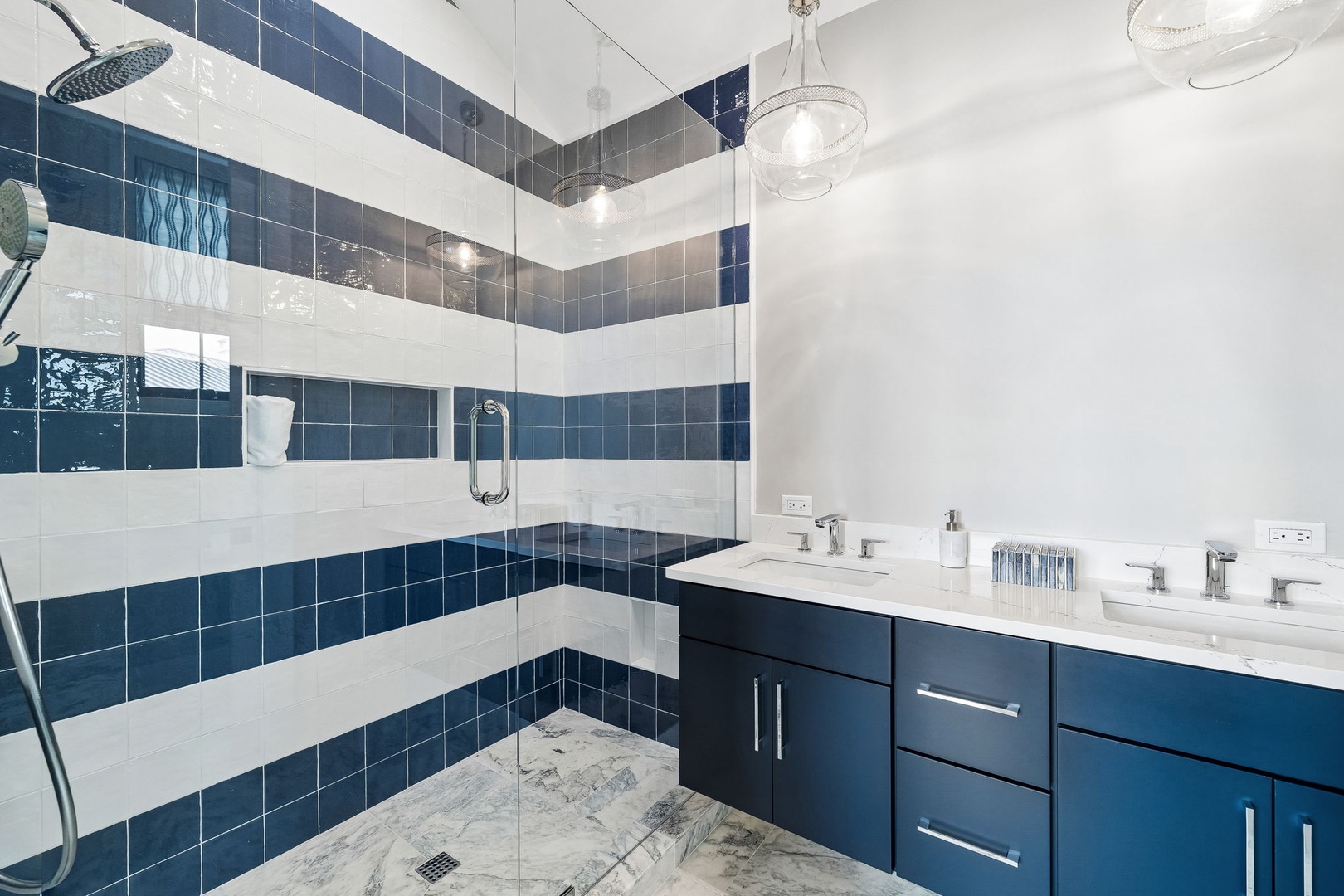 Refresh in your elegant walk-in shower with bold blue-and-white striped tile and a sleek rainfall showerhead. The dual-sink vanity offers ample space to unwind.