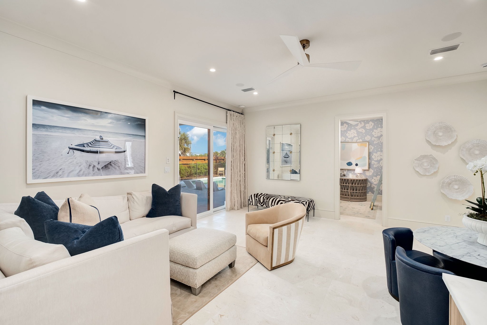 Your bright coastal-inspired living room welcomes you with plush seating and serene ocean artwork. Ceiling fan overhead keeps things comfortable while doors open to your private outdoor space.