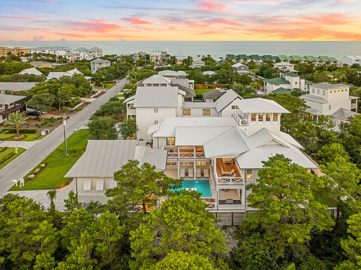 Spectacular coastal property set within lush green surroundings, just moments from the beach, with a private pool and expansive outdoor living spaces beneath a stunning sunset sky.