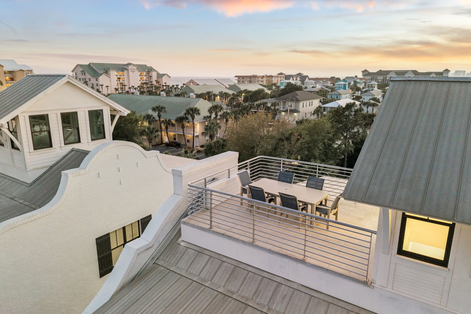 Elevated rooftop terrace features modern seating overlooking coastal neighborhood homes amid dramatic sunset skies.